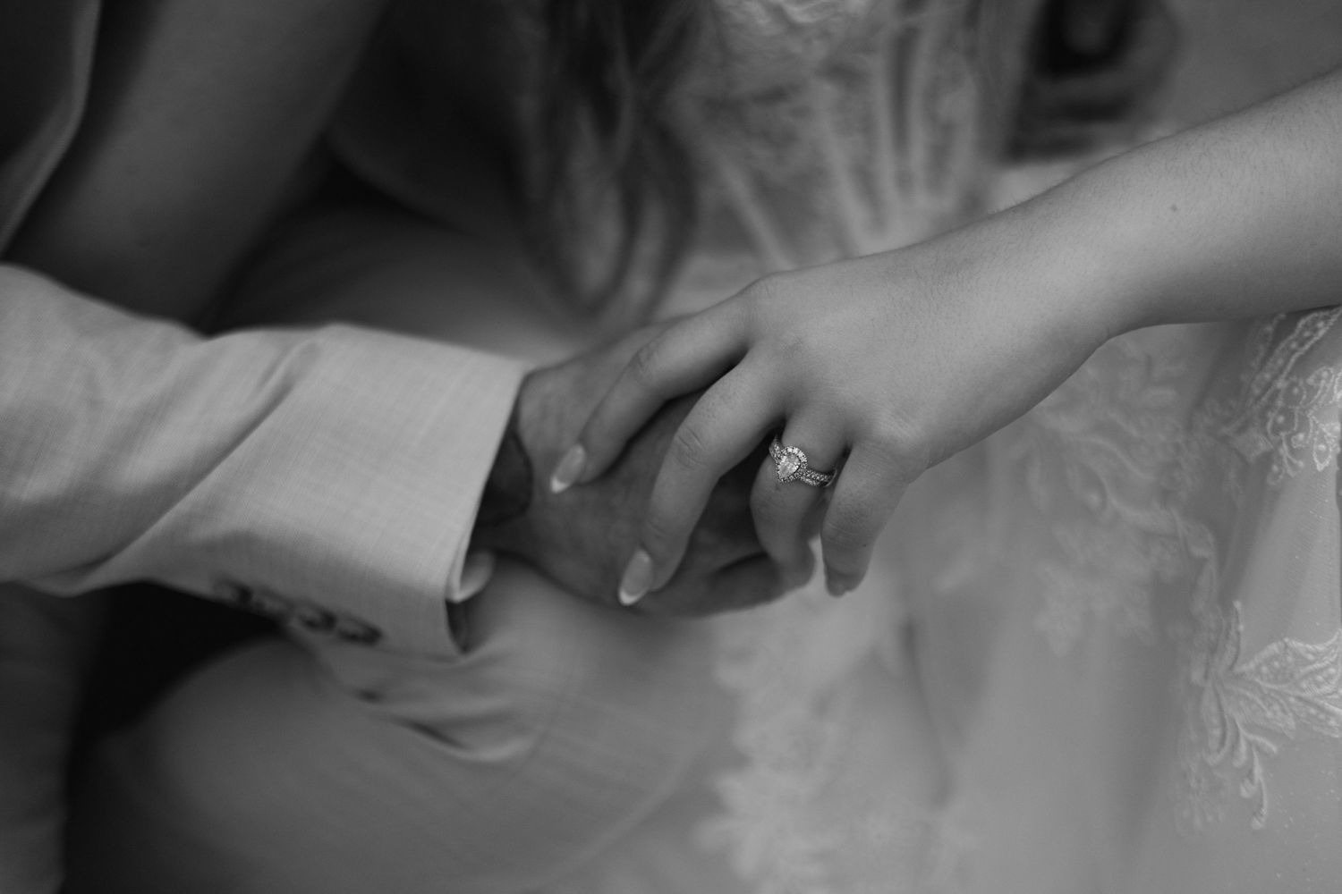 Close-up black and white photo of bride and groom holding hands, showing wedding ring.