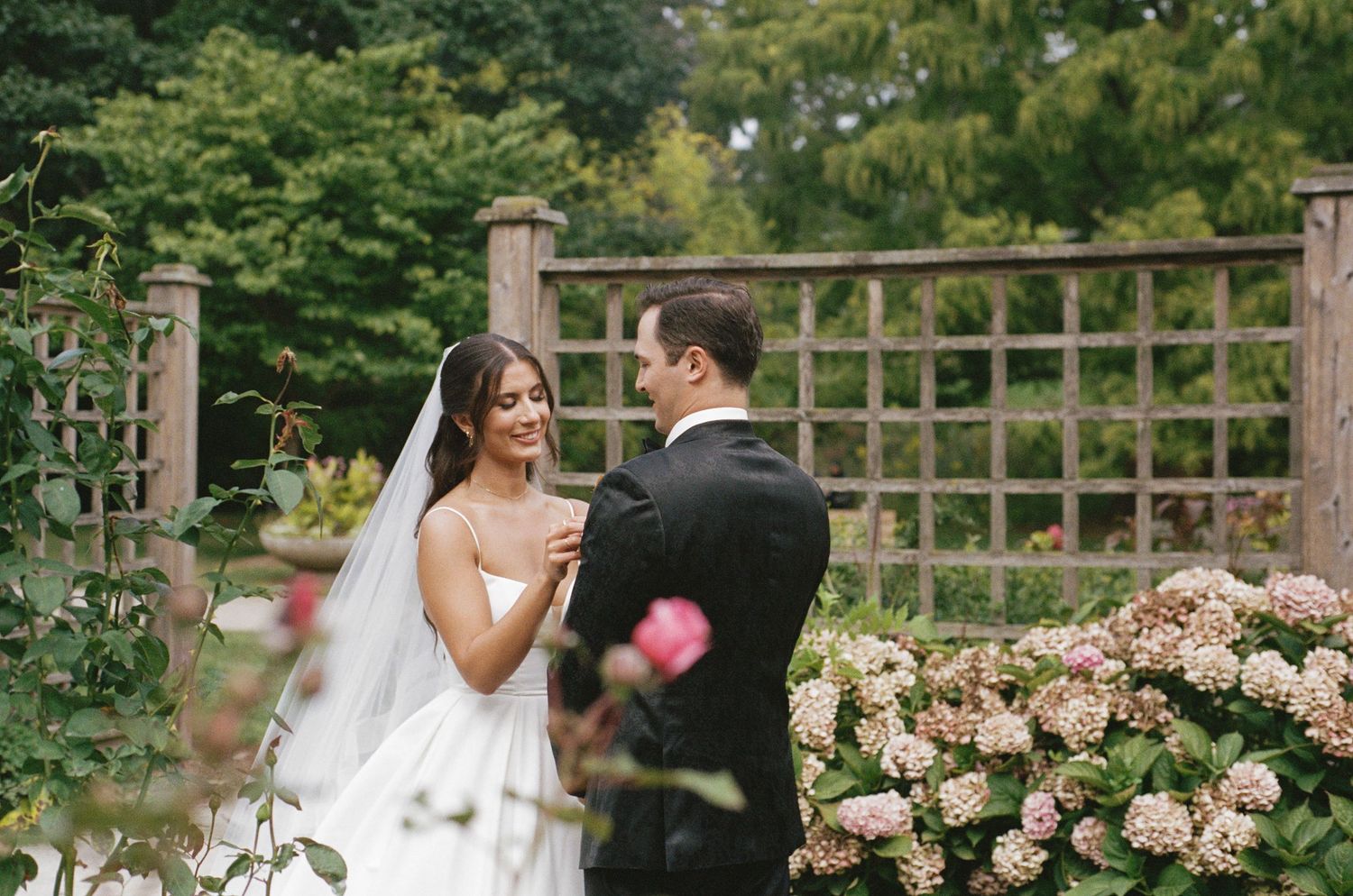 Bride and groom share a tender first look moment in a lush garden with hydrangeas.