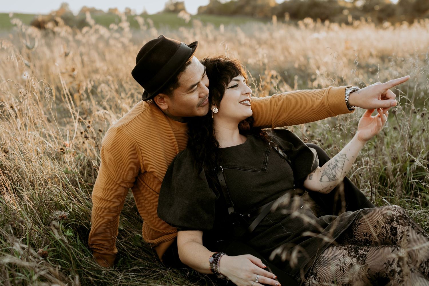 Happy couple sitting in a golden field, woman pointing at something in the distance.