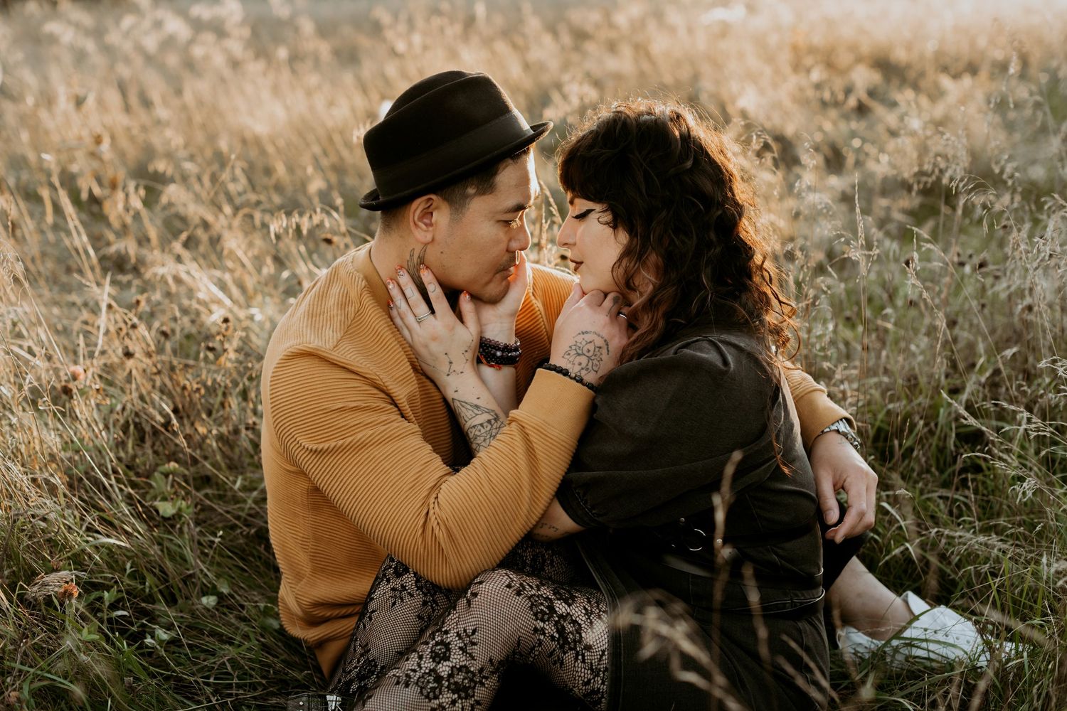 Couple sharing a tender moment sitting in a sunlit autumn field at golden hour.