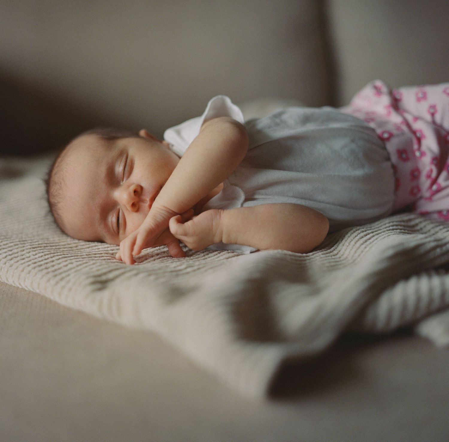 Peaceful newborn baby sleeping on textured cream blanket wearing white onesie and pink pants.