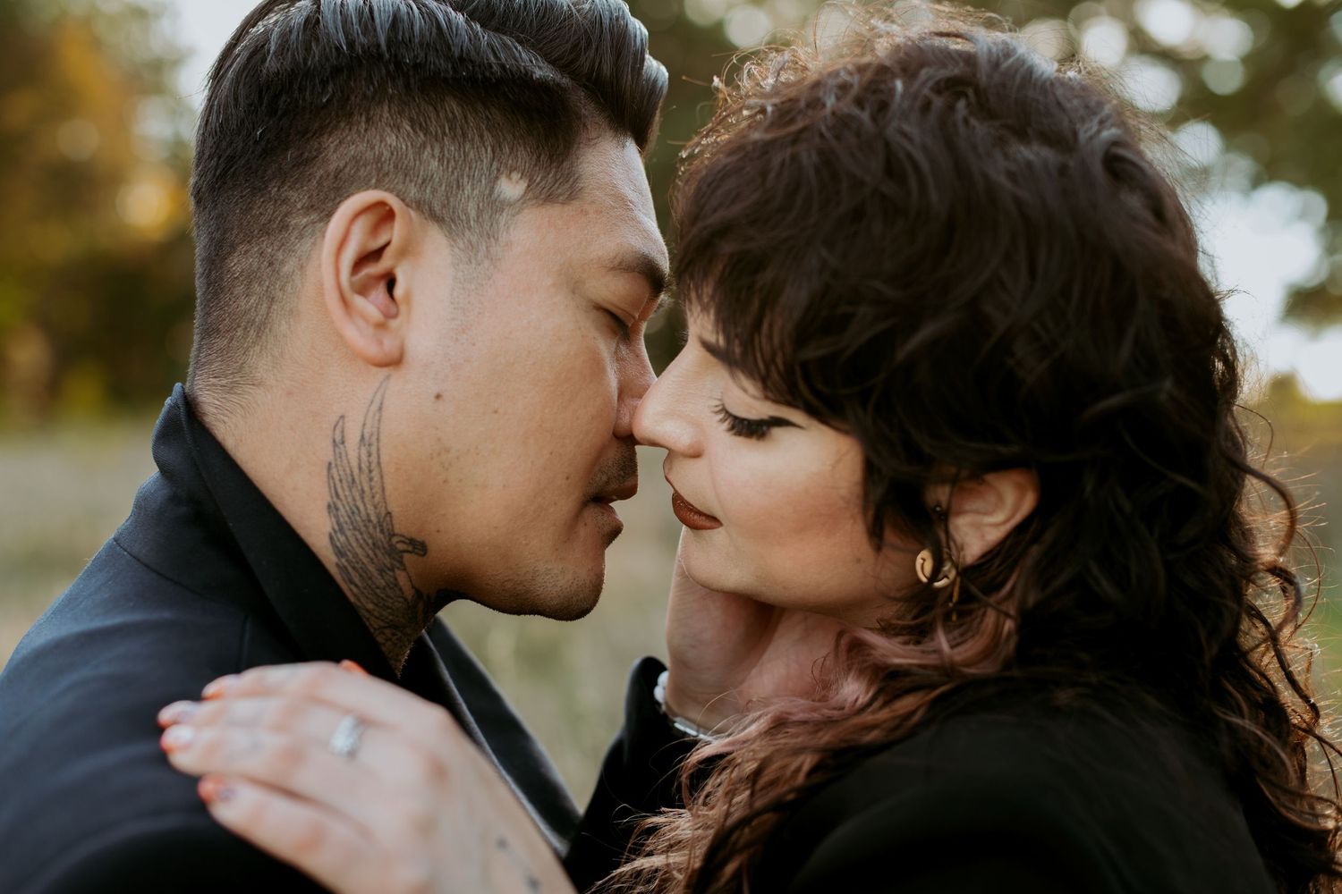 Close-up of a tattooed couple sharing an intimate almost-kiss outdoors.