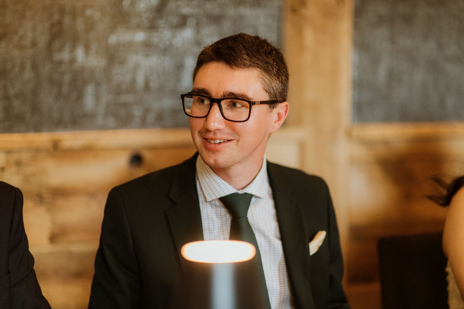 Man in dark suit and green tie smiling at wedding reception dinner.