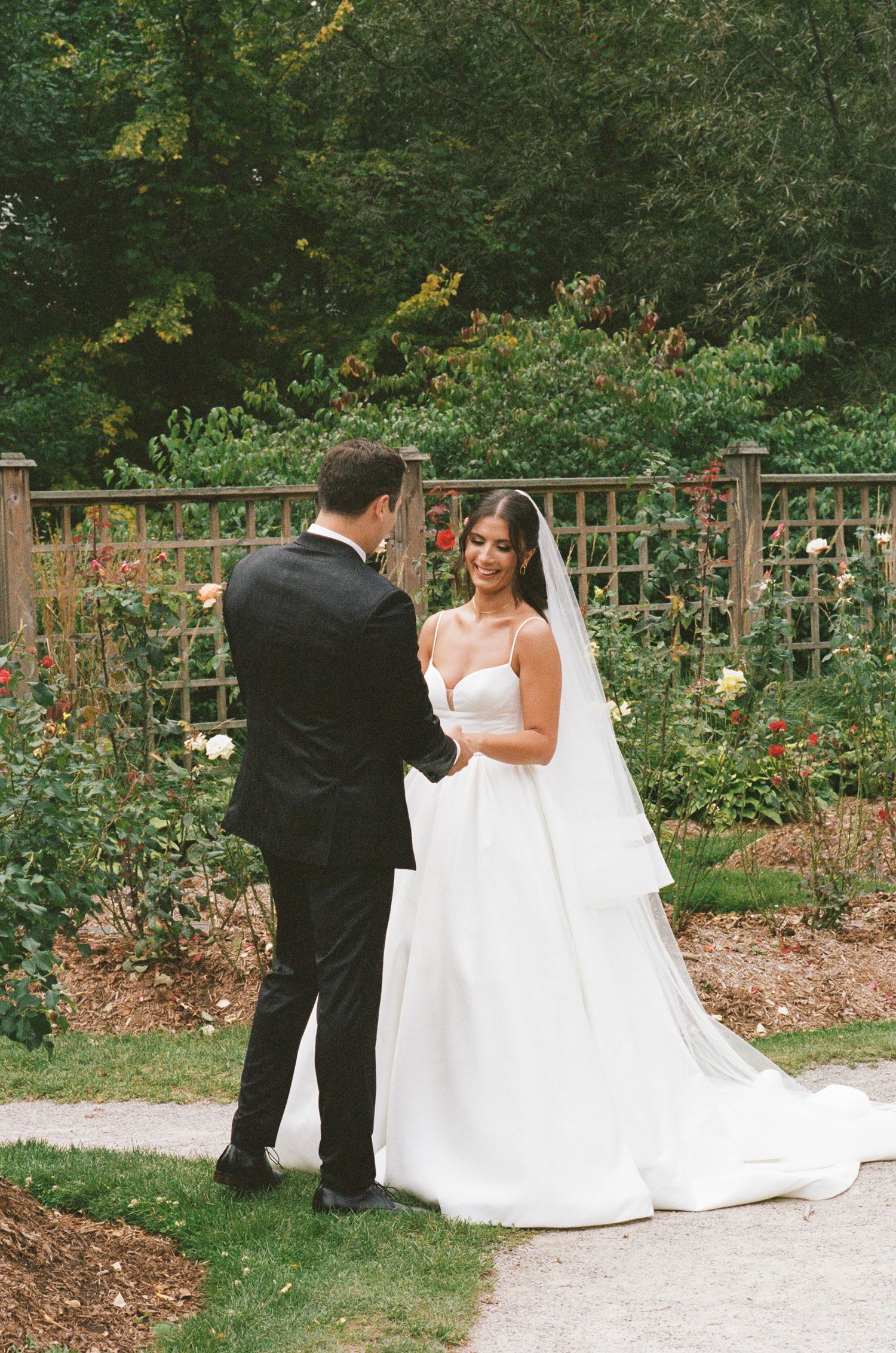 Bride and groom sharing a tender first look moment in a lush garden surrounded by roses.