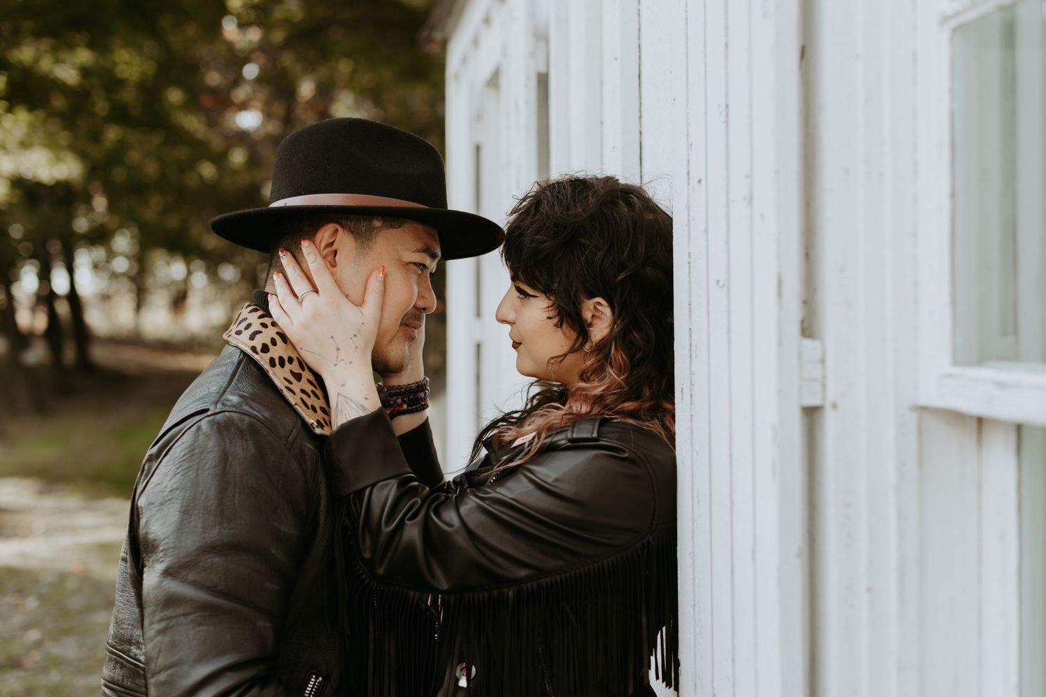 Intimate couple moment with woman tenderly holding mans face near a white building window.