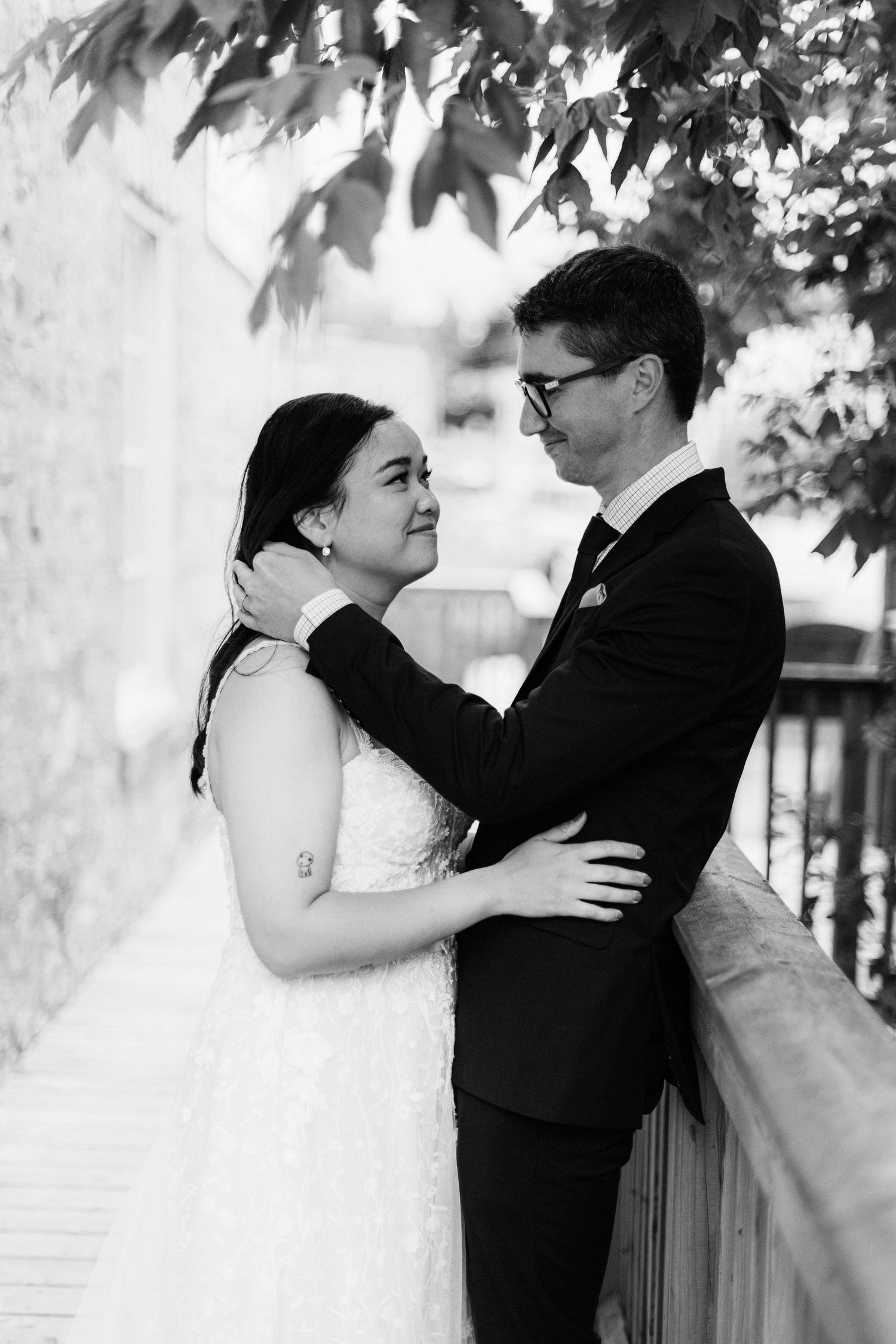Black and white portrait of bride and groom embracing tenderly on a wooden balcony outdoors.