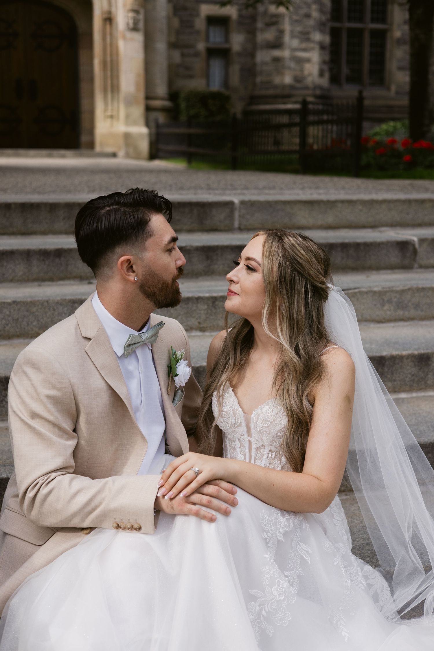 Bride and groom share an intimate moment on stone steps outside a historic building on their wedding day.