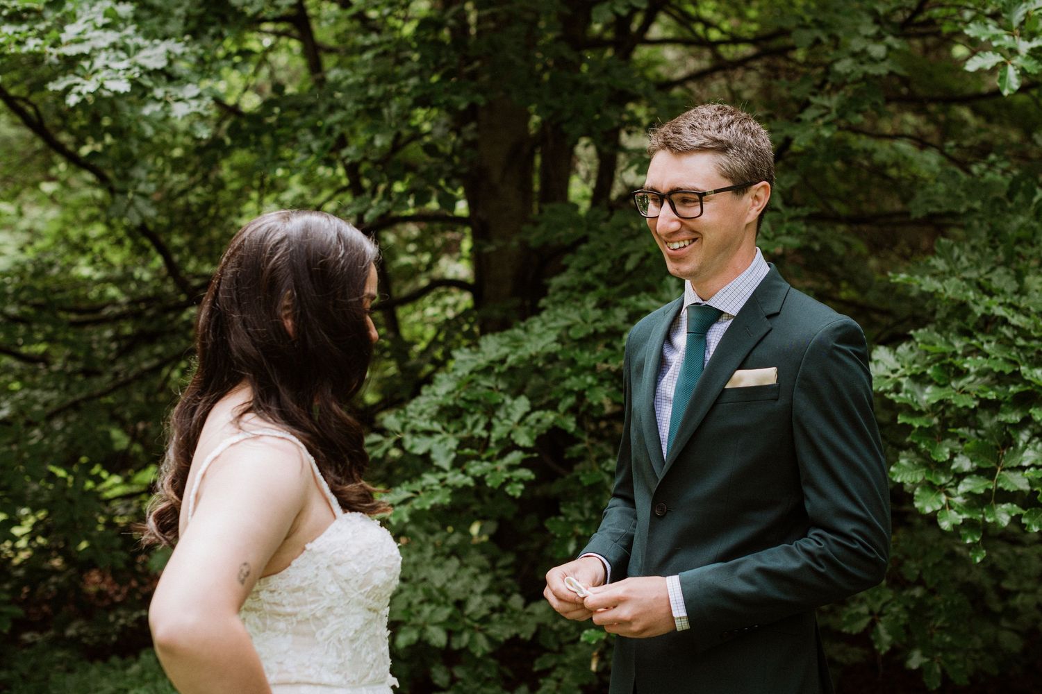 Groom in dark suit smiling at bride during outdoor first look wedding moment.