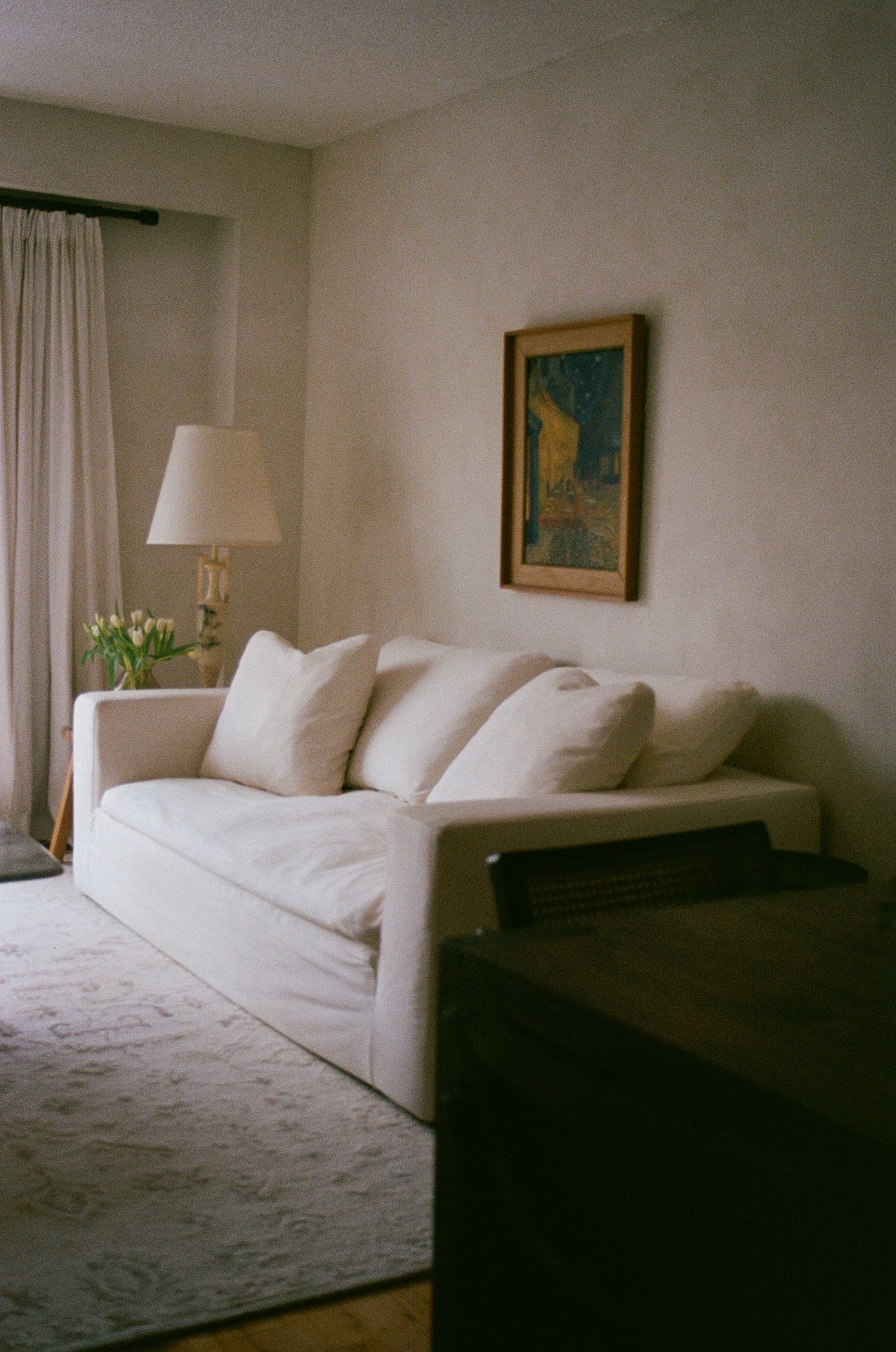 Bright living room with white slipcovered sofa, tulips, floor lamp, and framed Van Gogh print.