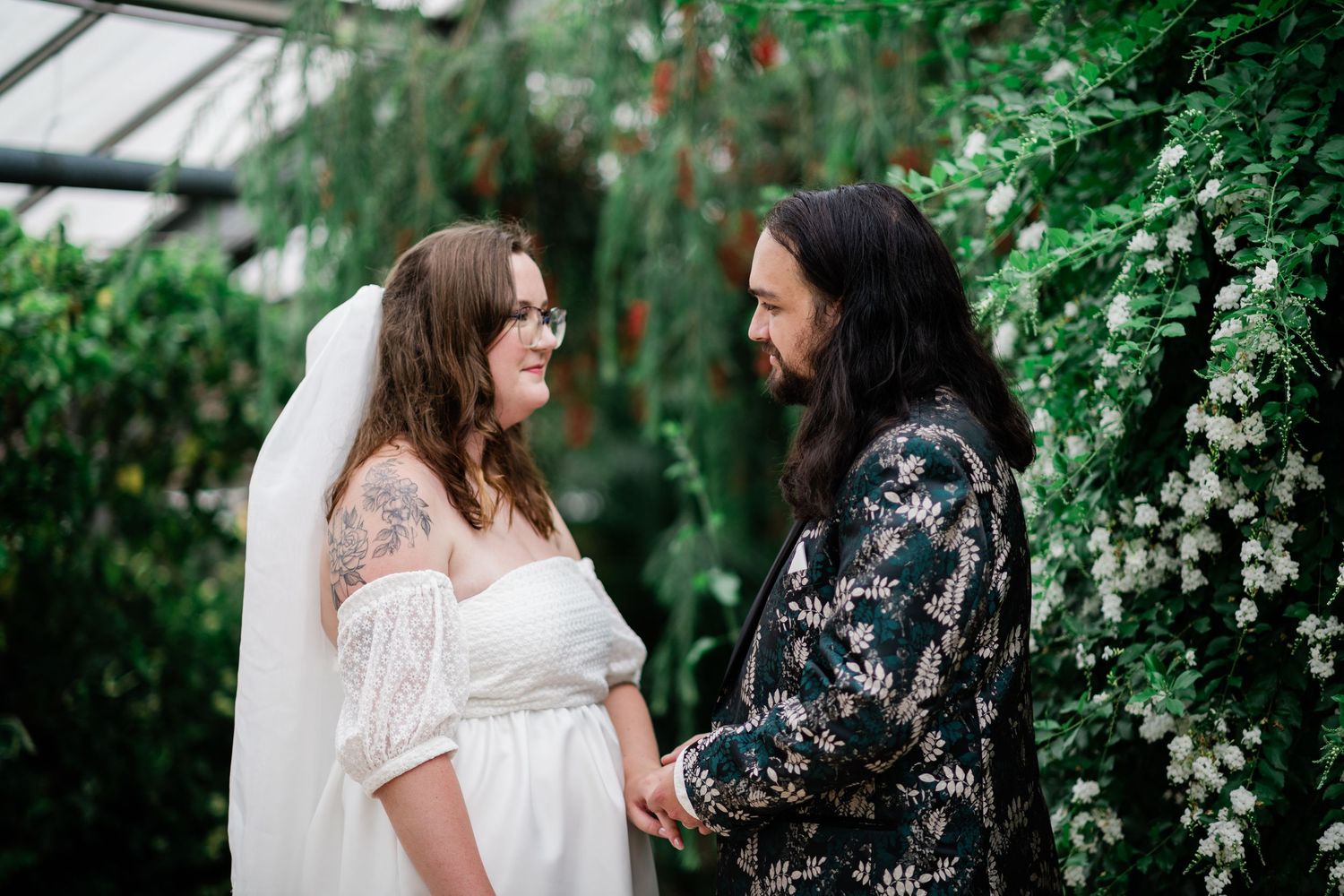 Couple holding hands in lush greenhouse wedding ceremony surrounded by greenery.