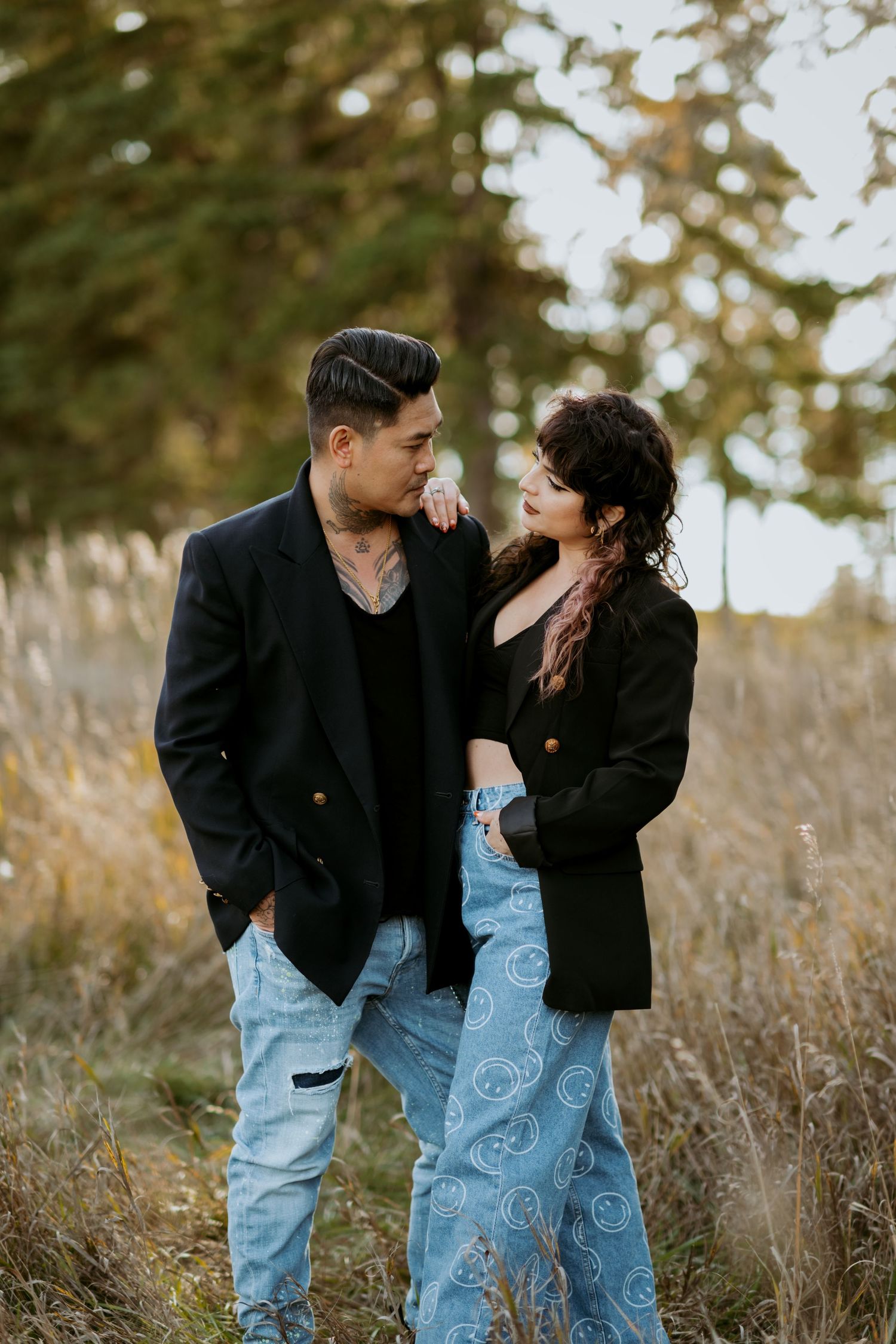 Couple in matching black blazers and jeans sharing a romantic moment in a golden autumn field.