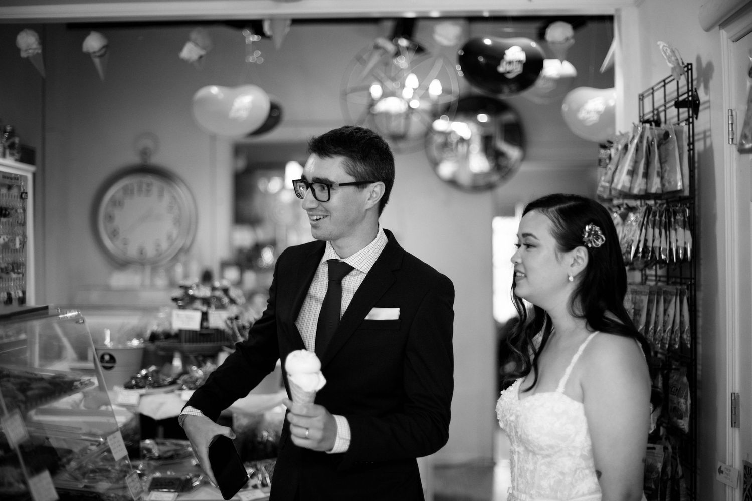 Bride and groom smiling while enjoying ice cream inside a charming shop, black and white photo.