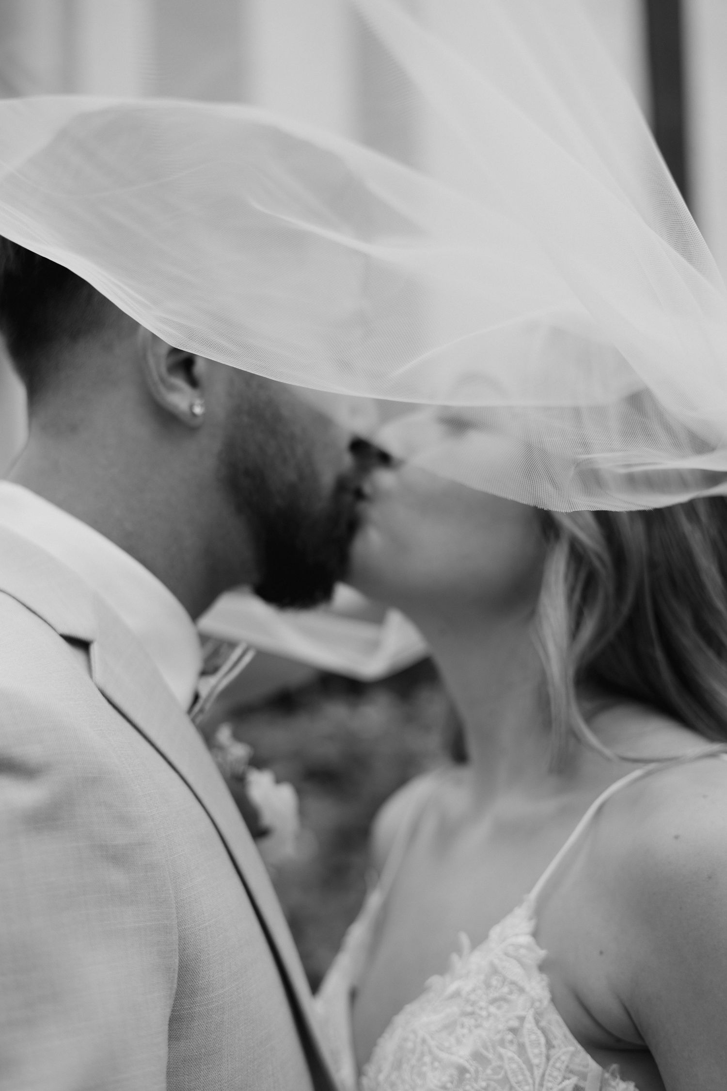 Black and white romantic photo of bride and groom kissing under flowing bridal veil.