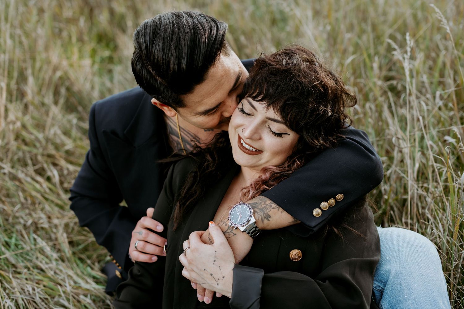 Man embracing woman from behind as she smiles in a golden grass field.