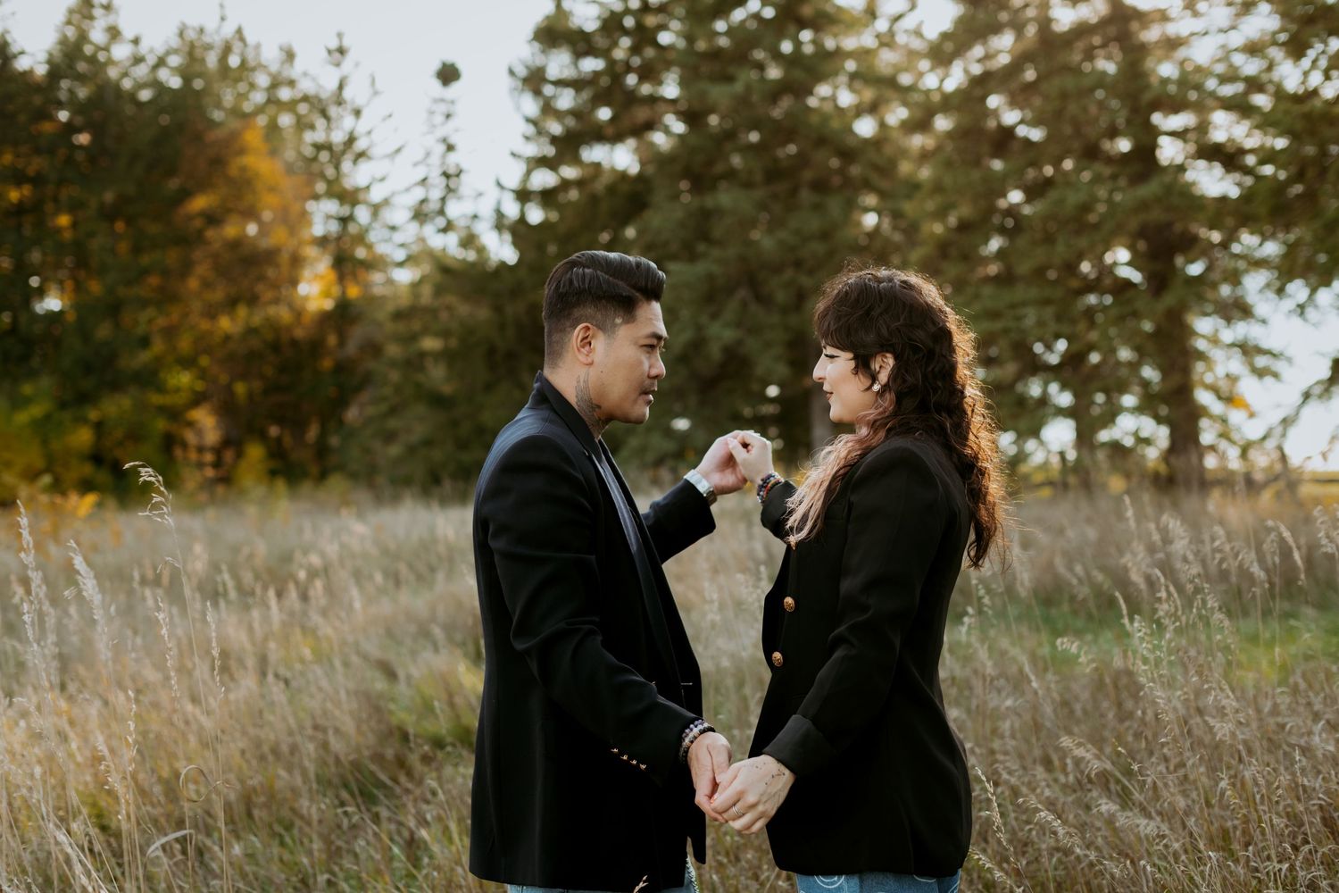Couple holding hands and facing each other in an autumn field with tall grass.