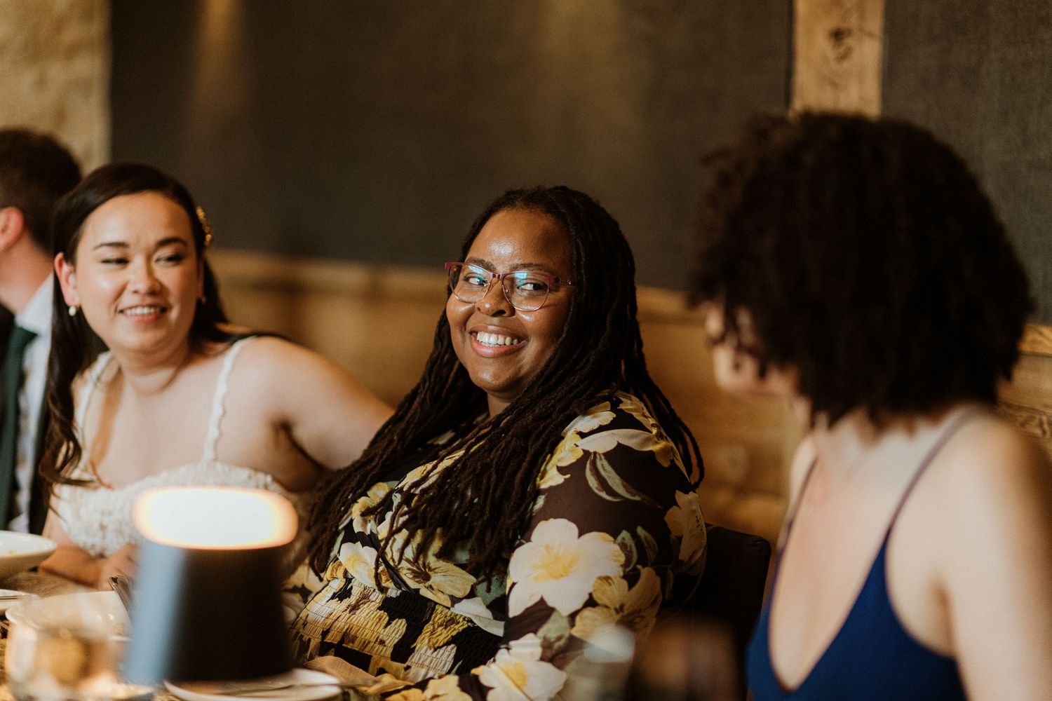 Two women smiling and laughing together at a wedding reception dinner table.