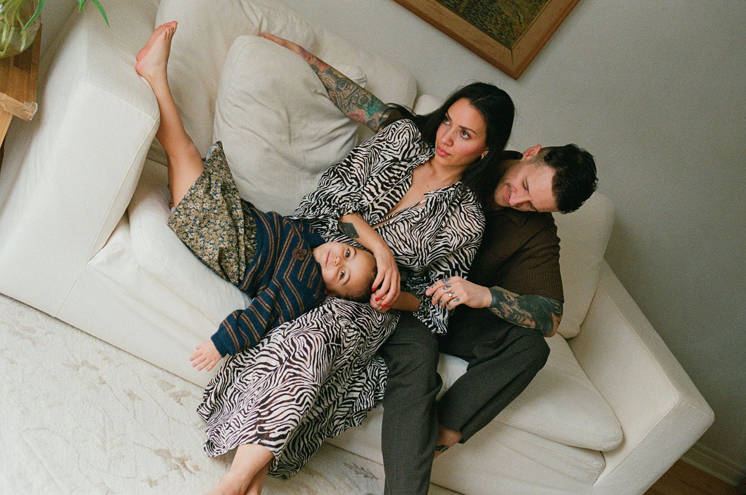 Aerial view of family of three relaxing together on a white couch at home.