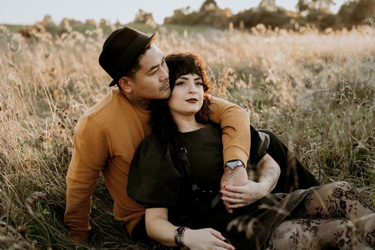 Couple cuddling in a sunlit golden field, man in hat embracing woman in green.