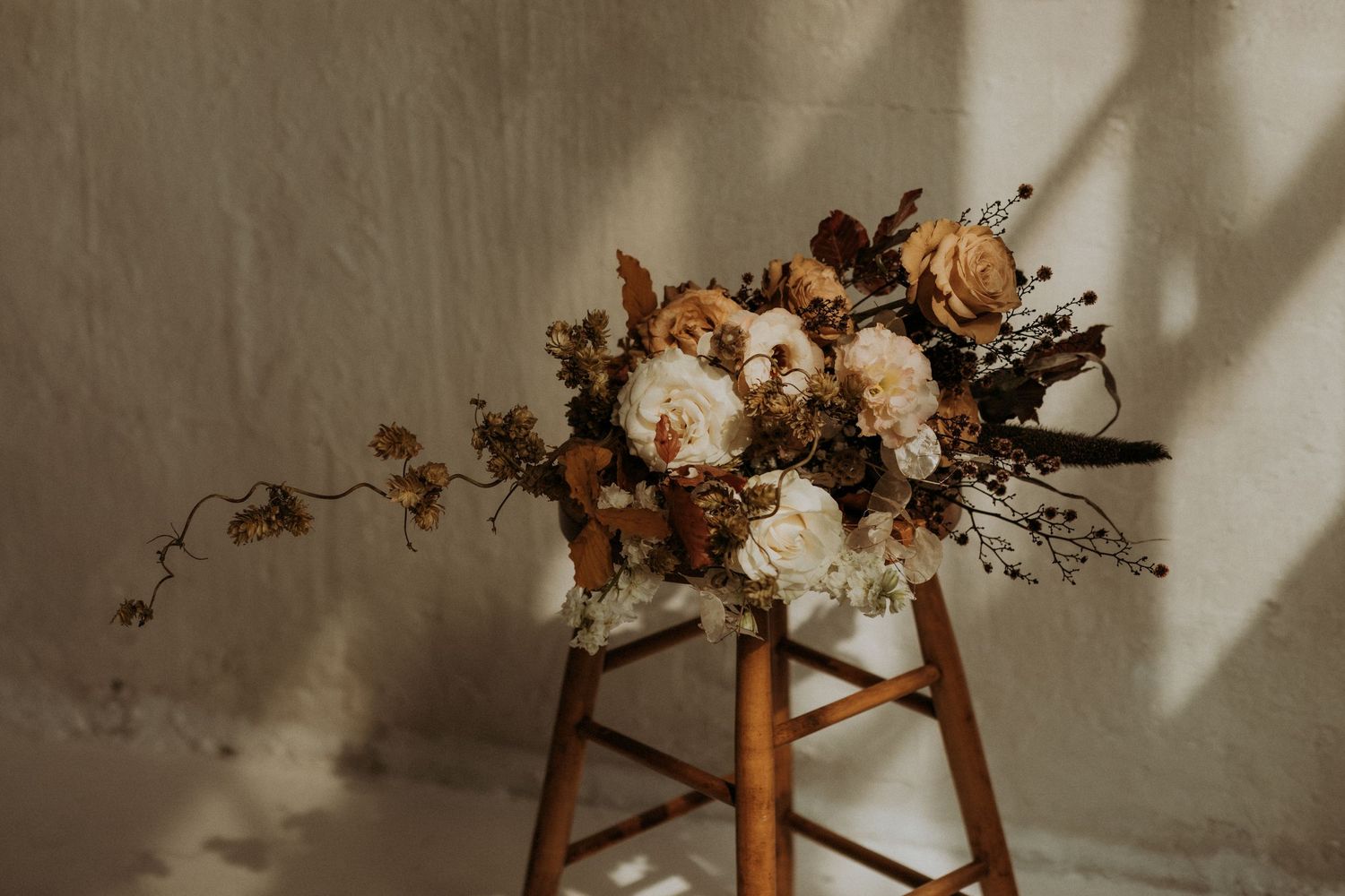 Elegant bridal bouquet with cream peonies and rust dried flowers on wooden stool.