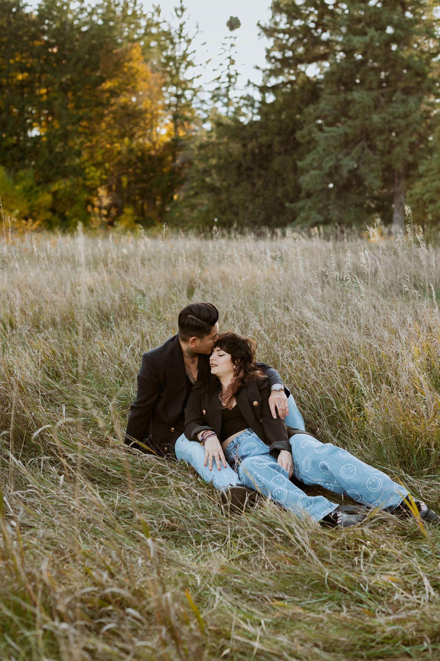 Couple relaxing together in tall grass field with autumn trees in background.