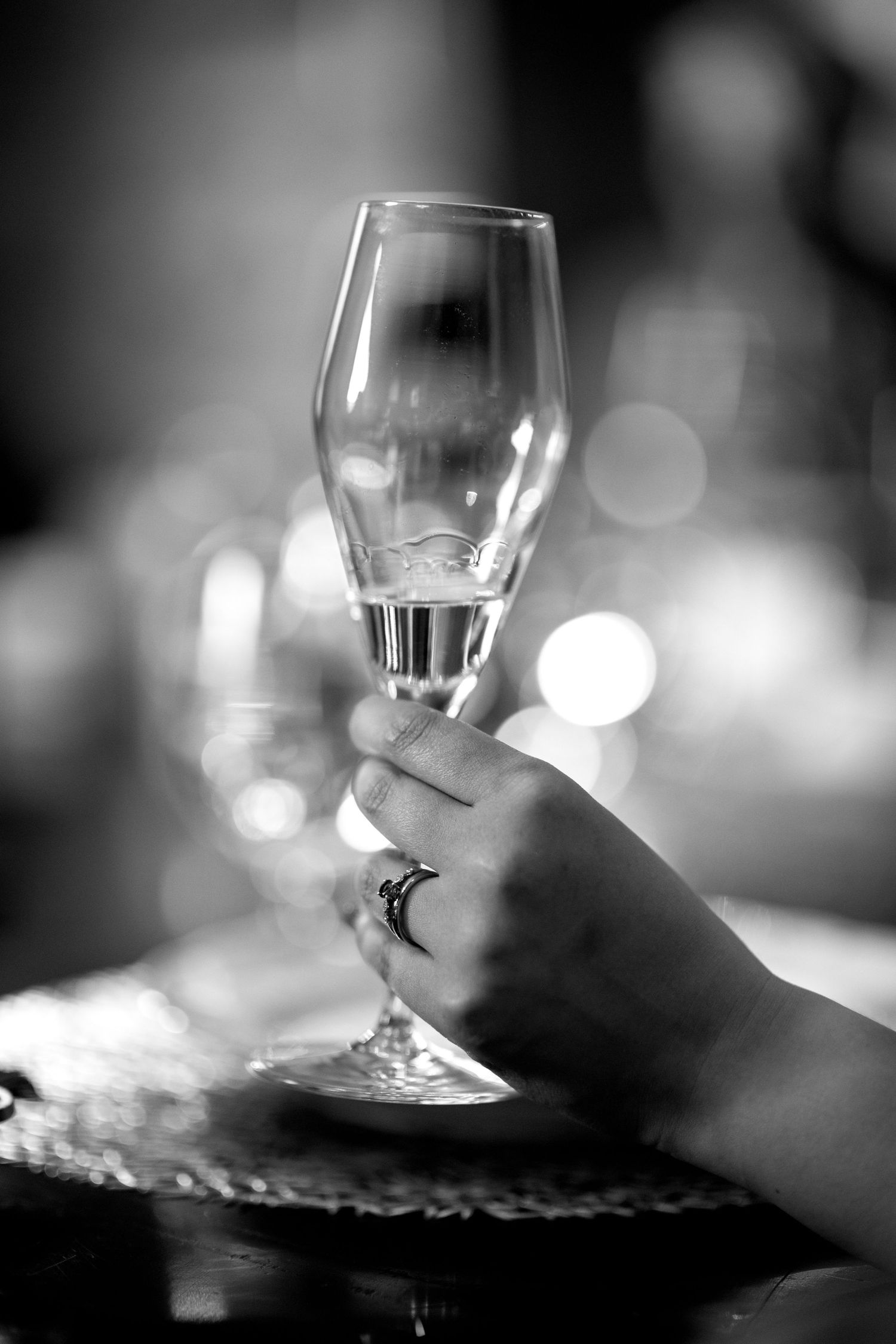 Close-up black and white photo of hand holding champagne flute at wedding reception.