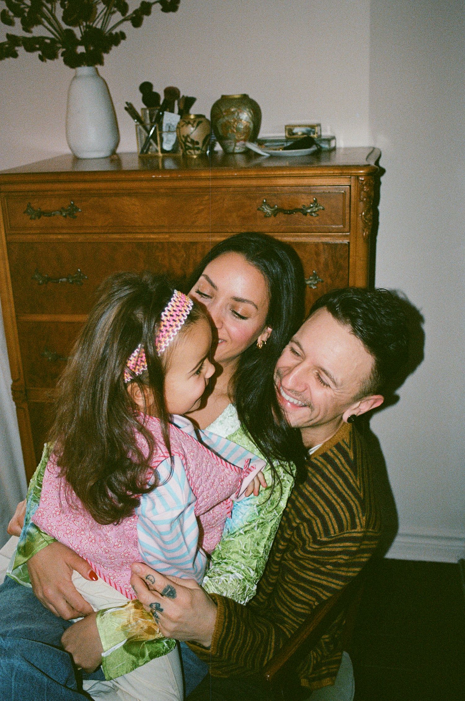 A loving family shares a tender embrace, with a mother kissing her child while a smiling man looks on.