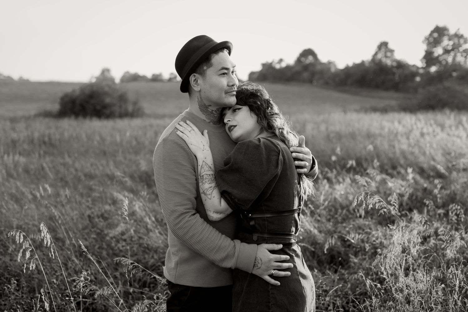 Black and white photo of couple embracing tenderly in a grassy field, woman resting head on mans chest.