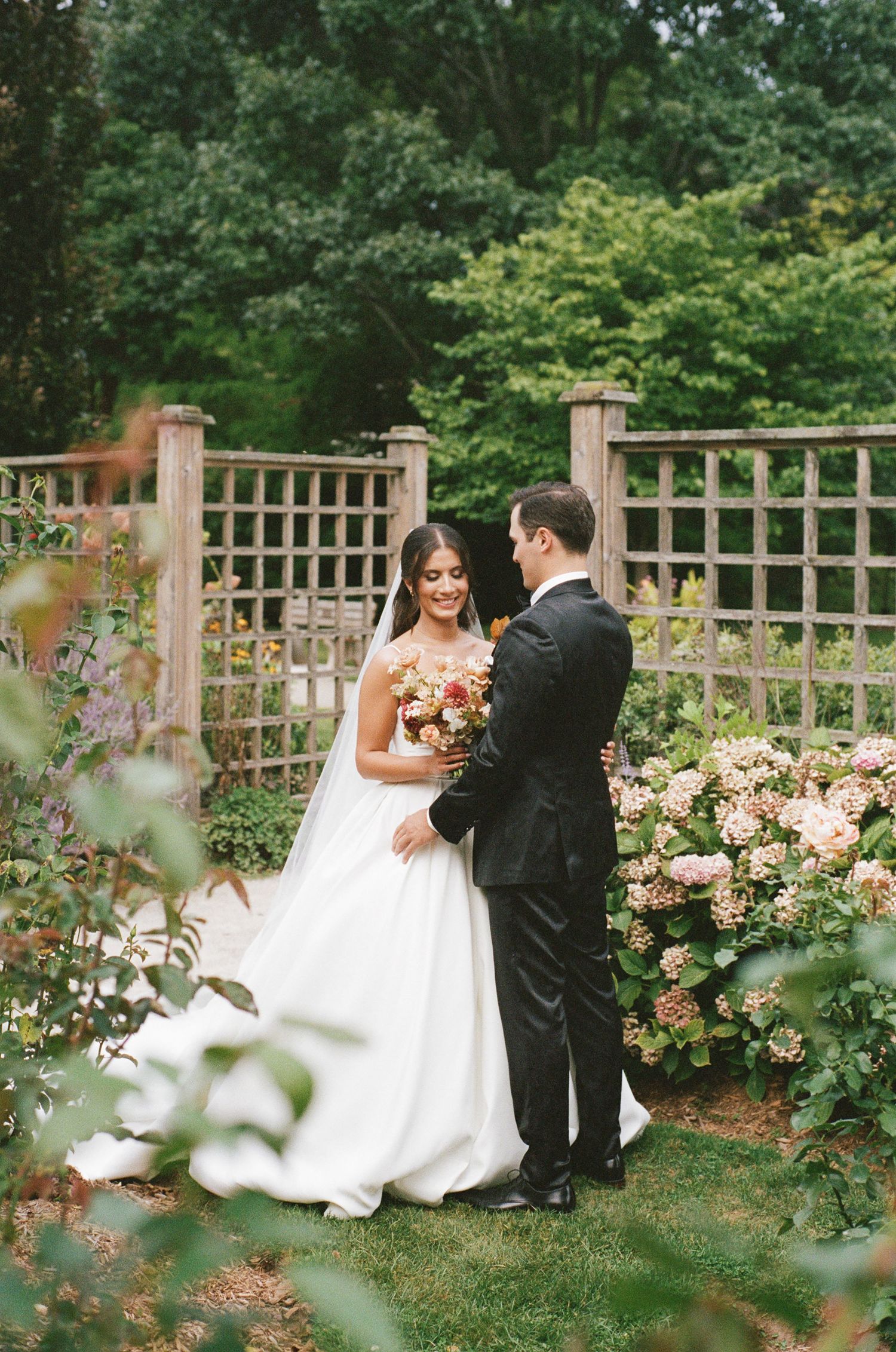 Bride and groom share an intimate moment in a lush garden surrounded by blooming hydrangeas.