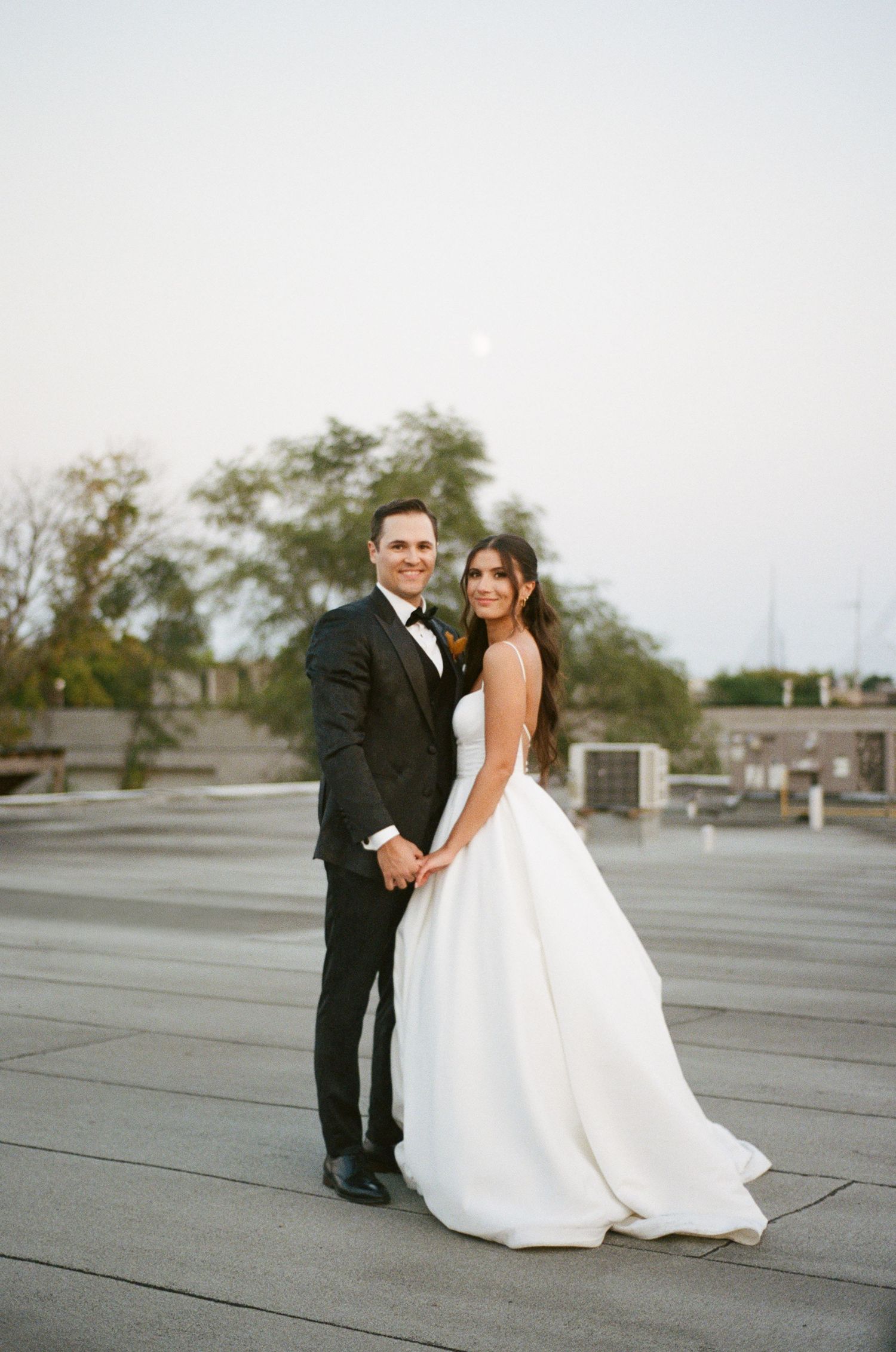 Elegant bride and groom posing together on rooftop under moonlit sky in classic wedding attire.