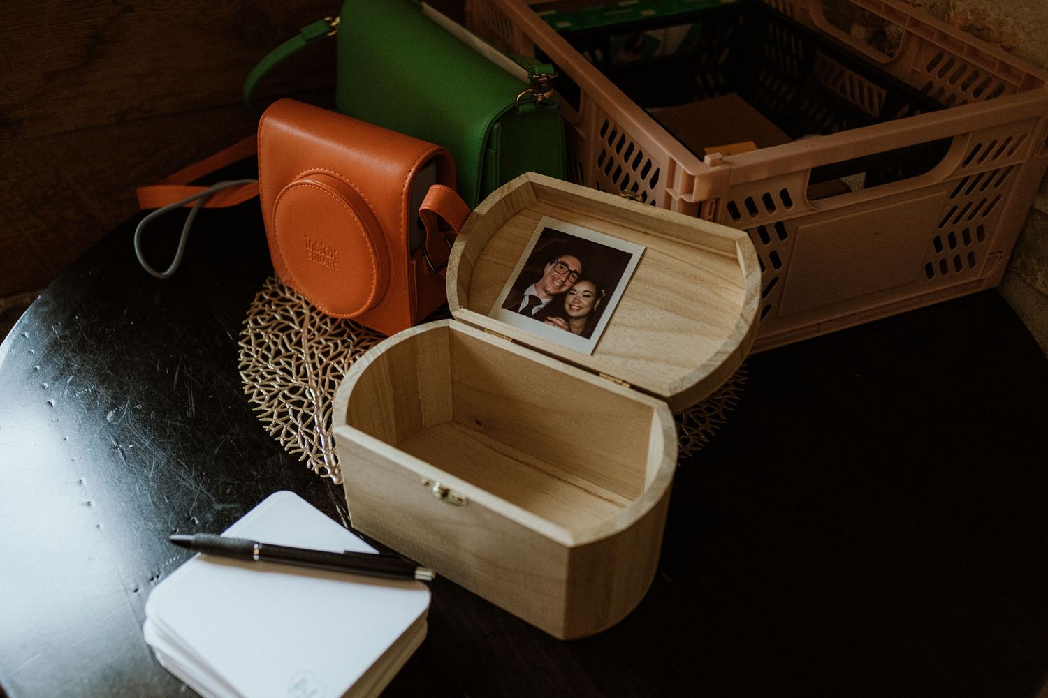 Close-up of wooden keepsake box with couple photo inside, Instax camera and notepad on dark table.