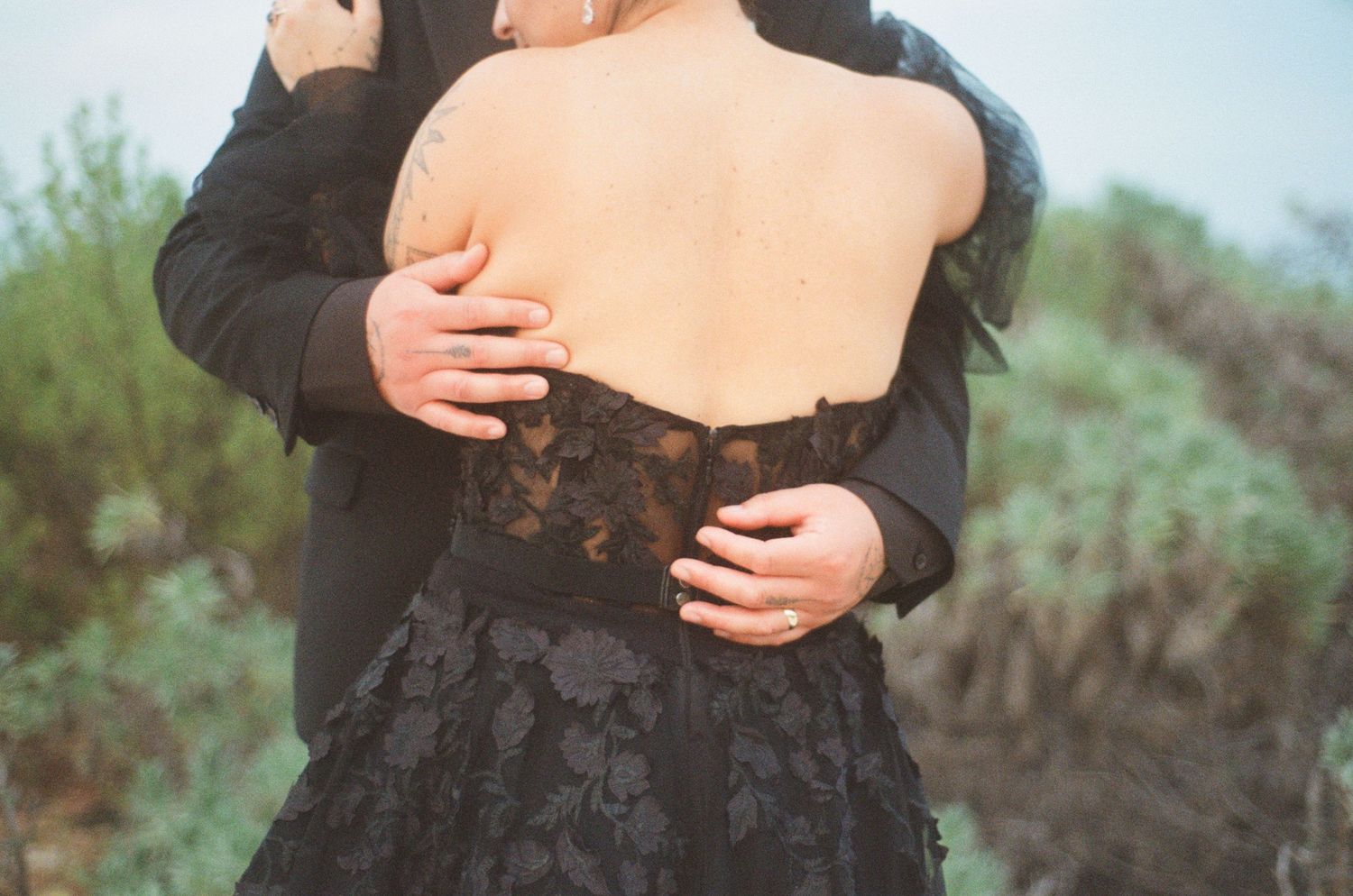 Close-up of groom embracing bride in black lace backless wedding gown outdoors.