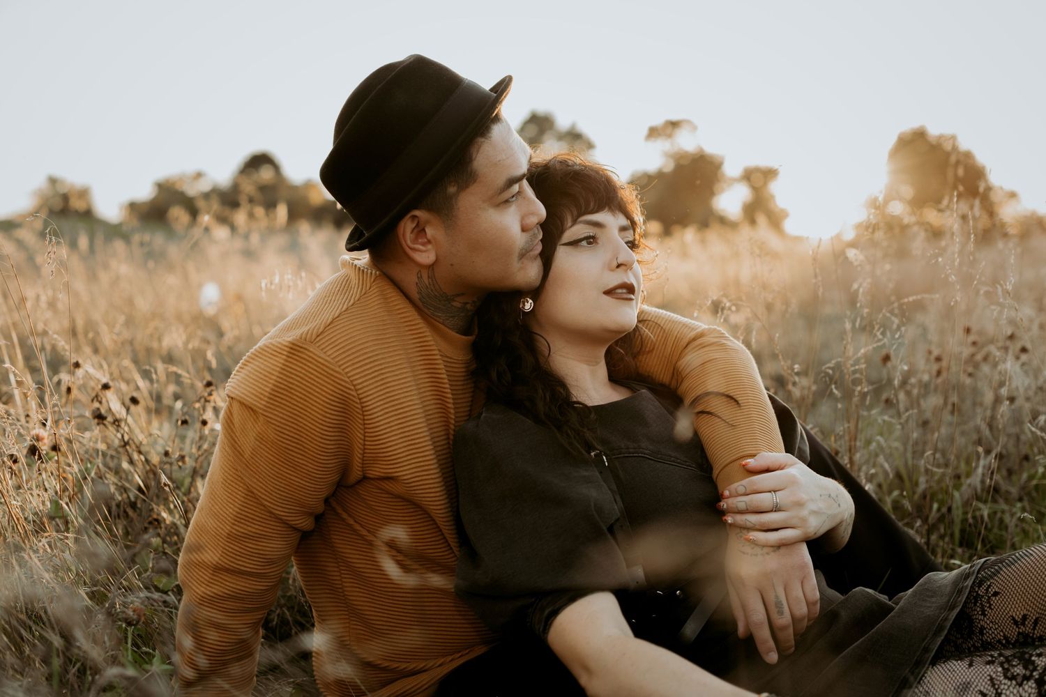 Romantic couple sitting together in a sunlit golden field during warm sunset light.