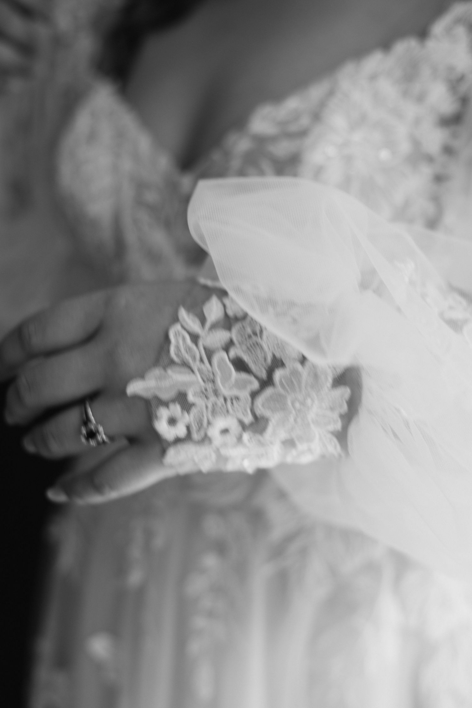 Black and white close-up of bride's lace wedding dress bodice and veil with ring detail.