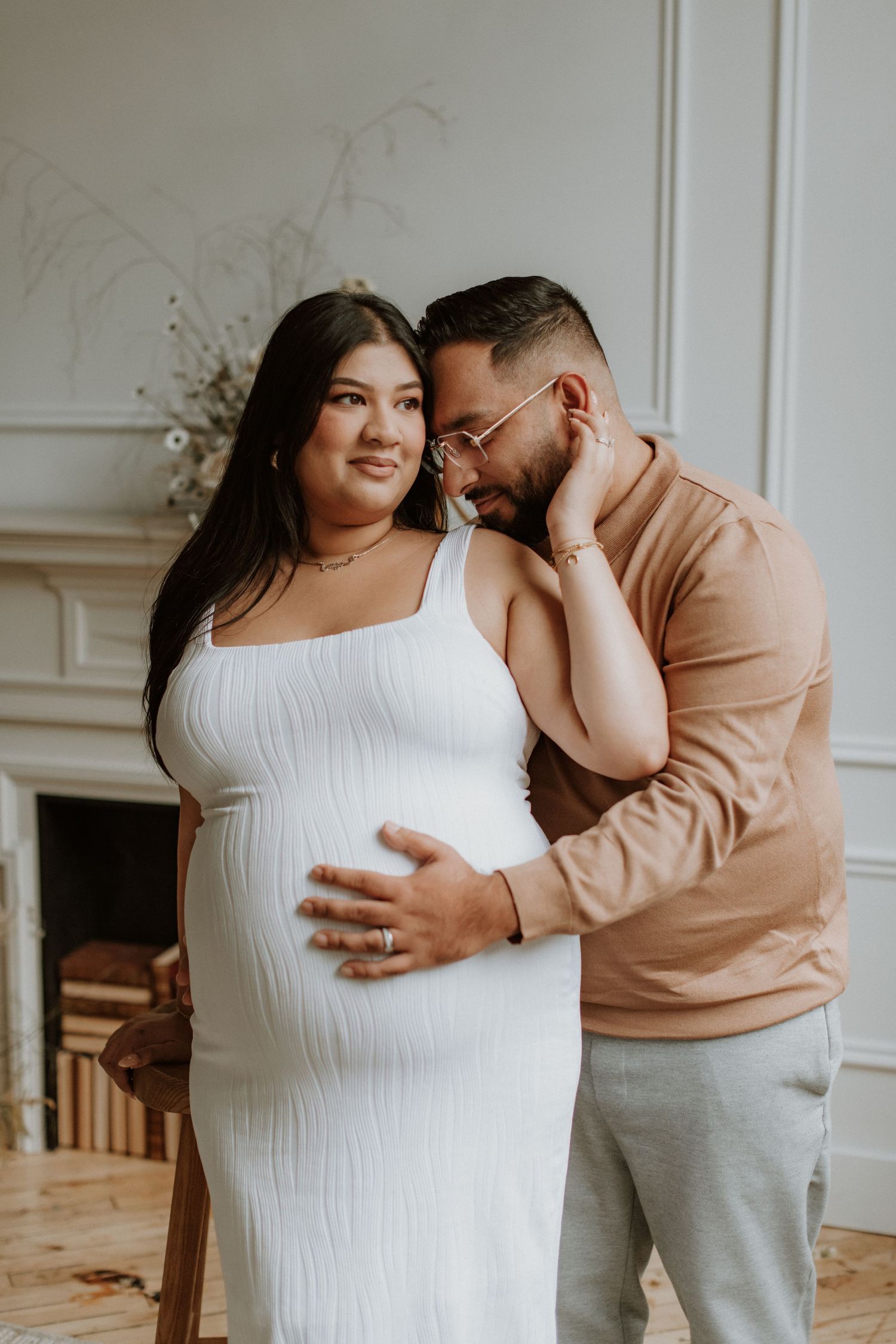 Expectant couple embracing tenderly in white studio room during intimate indoor maternity photography session.