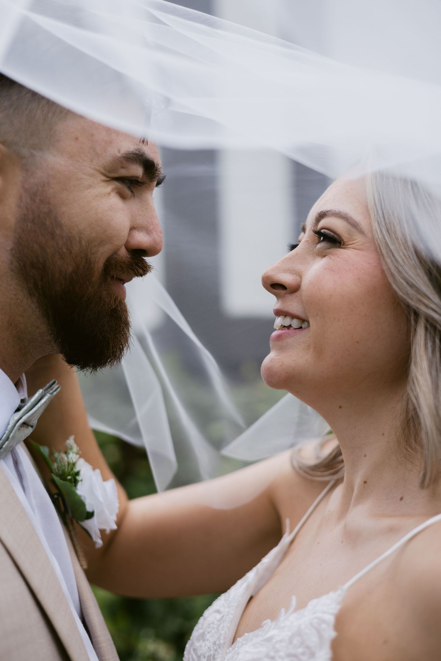 Close-up of smiling bride and groom gazing at each other under bridal veil on wedding day.
