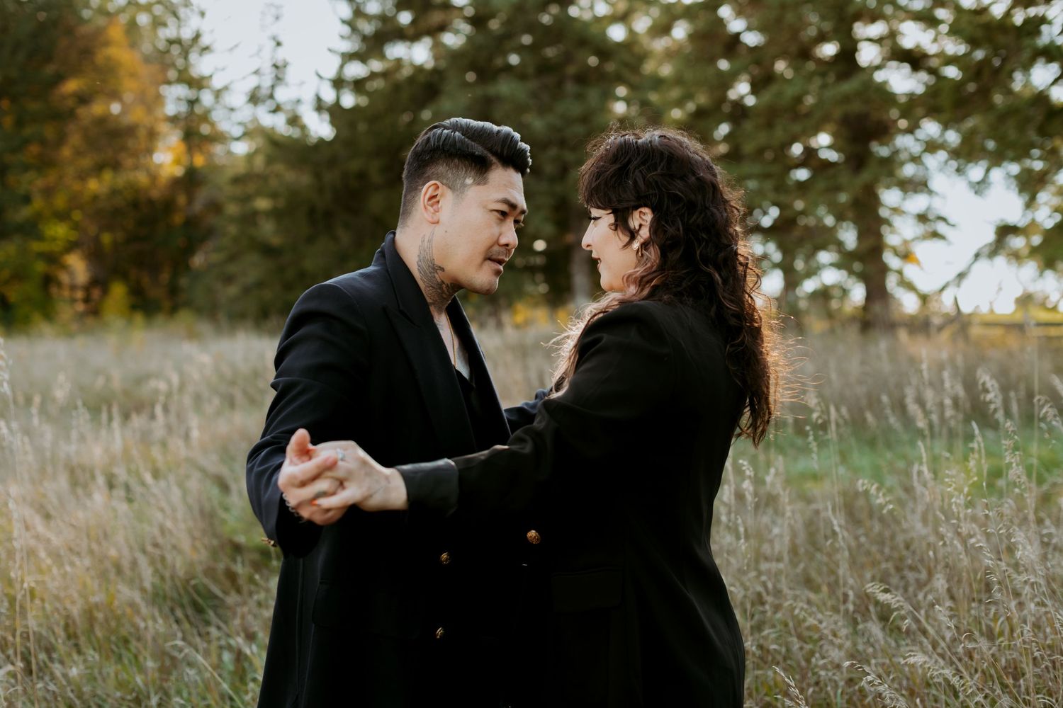 A couple in black outfits dancing and smiling together in a golden autumn meadow.