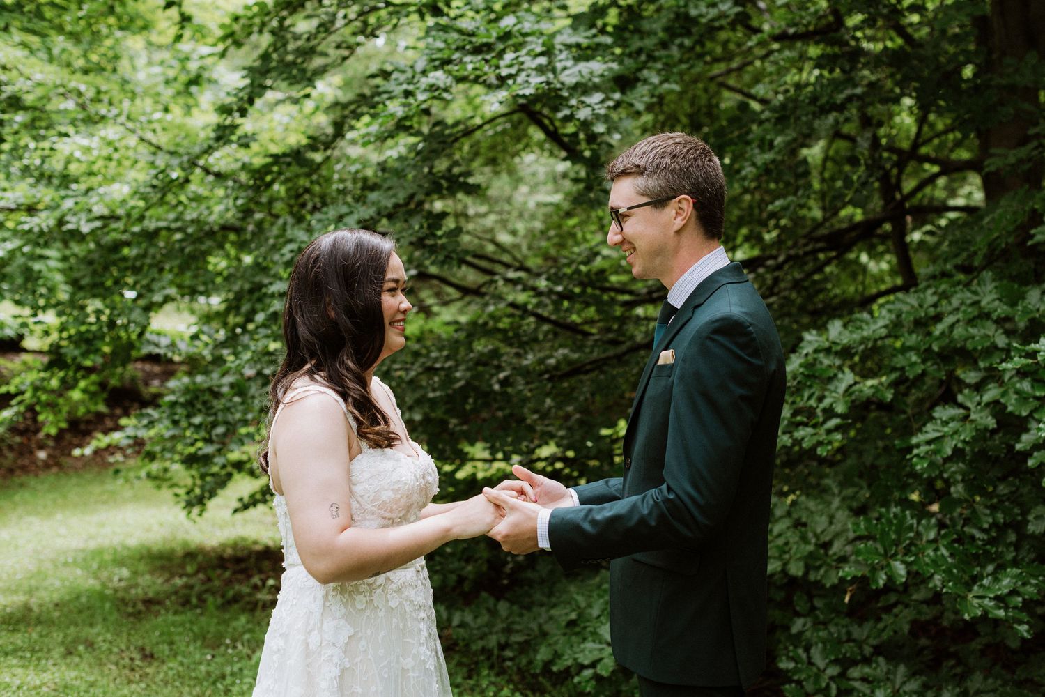 Bride and groom holding hands and smiling during outdoor first look ceremony.