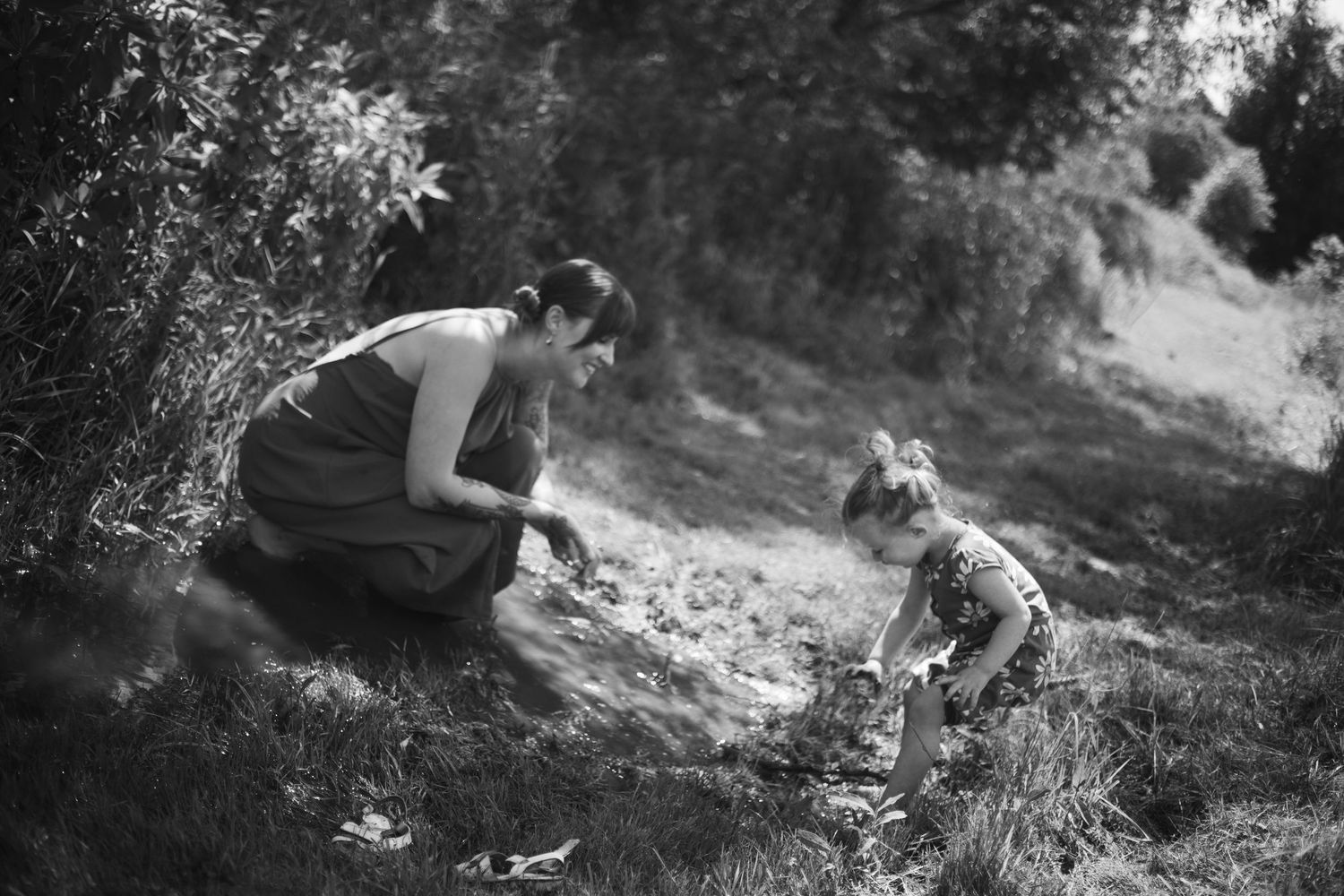 Black and white photo of mother and toddler daughter playing together on grassy hillside outdoors.