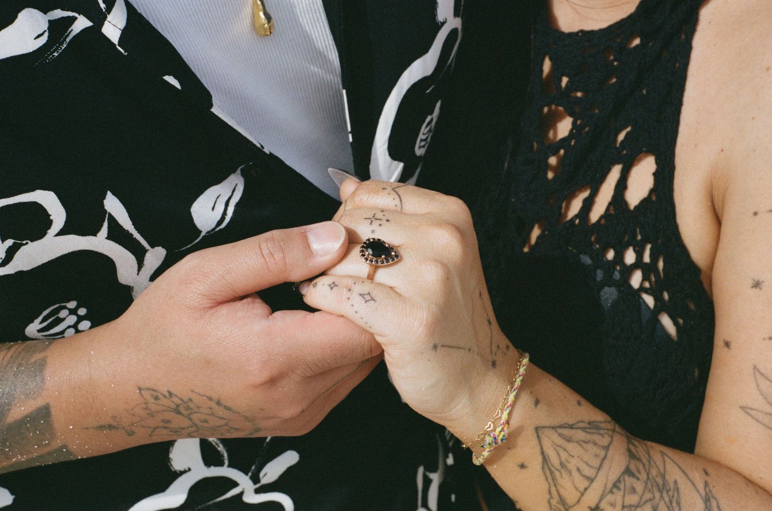 Close-up of tattooed hands with an engagement ring being placed on finger, both wearing black outfits.