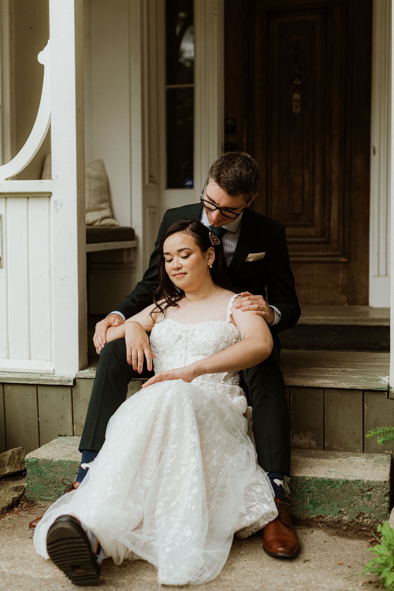 Wedding couple sharing intimate moment on stone steps, bride in white lace dress, groom in black suit.