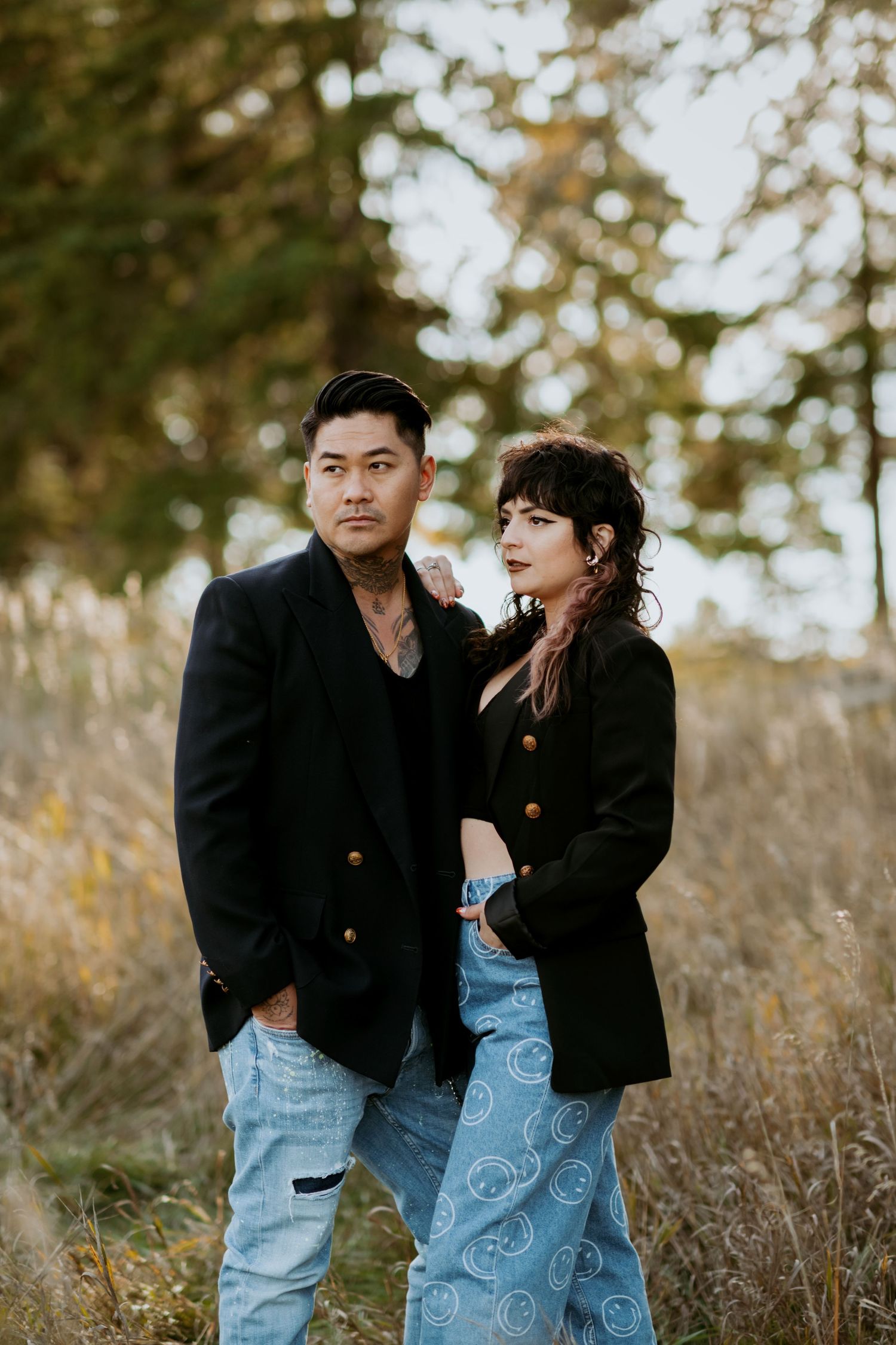 Stylish couple in black blazers posing seriously together in a fall outdoor setting with tall grass.