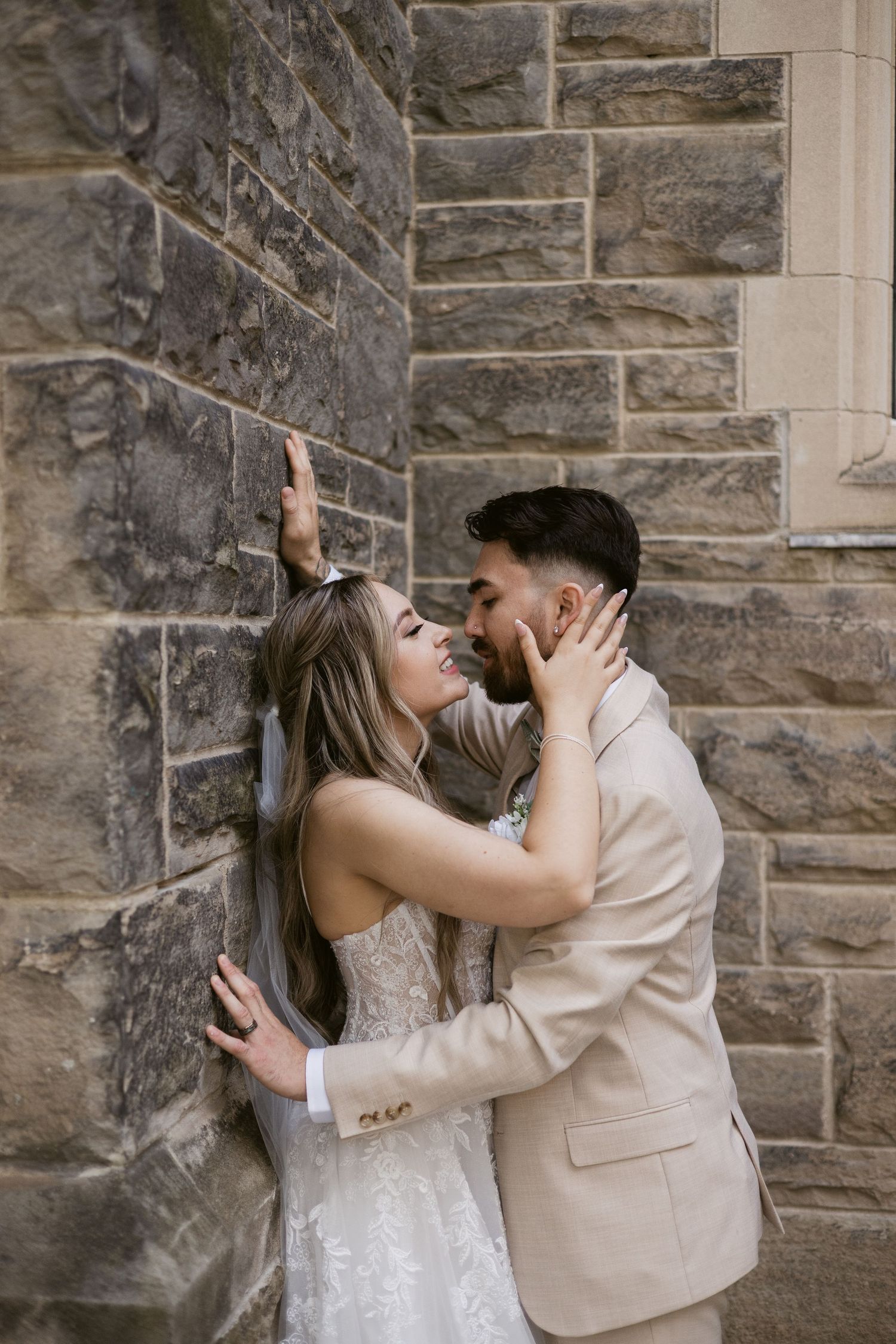 Bride and groom share a romantic almost-kiss against rustic stone wall during outdoor wedding portraits.