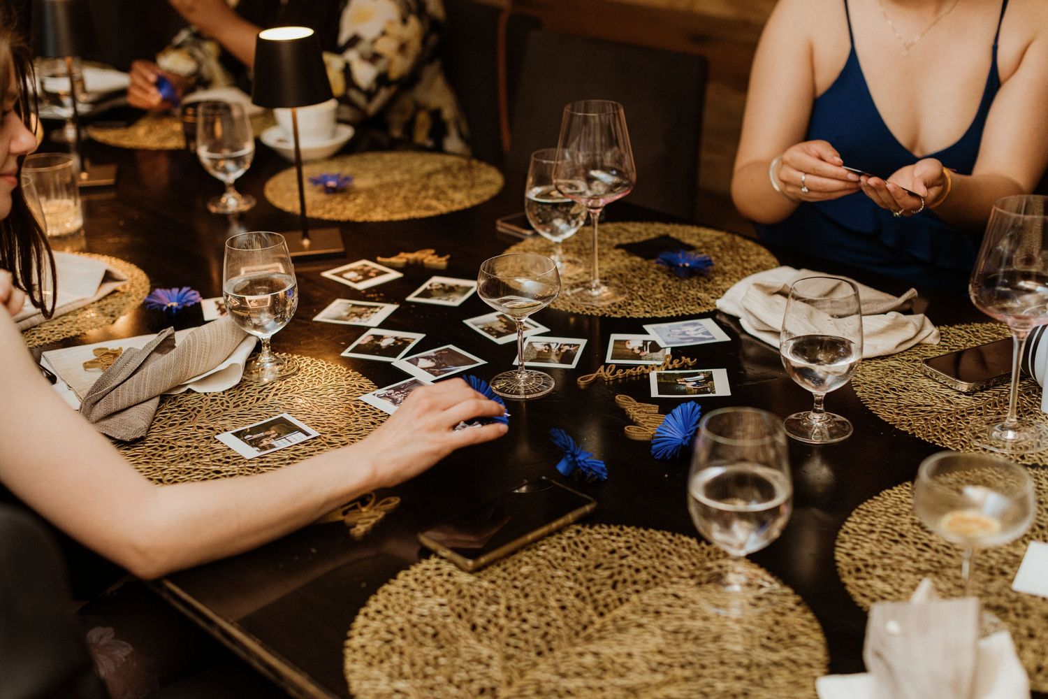 Wedding guests browse Polaroid photos spread across decorated reception dinner table.