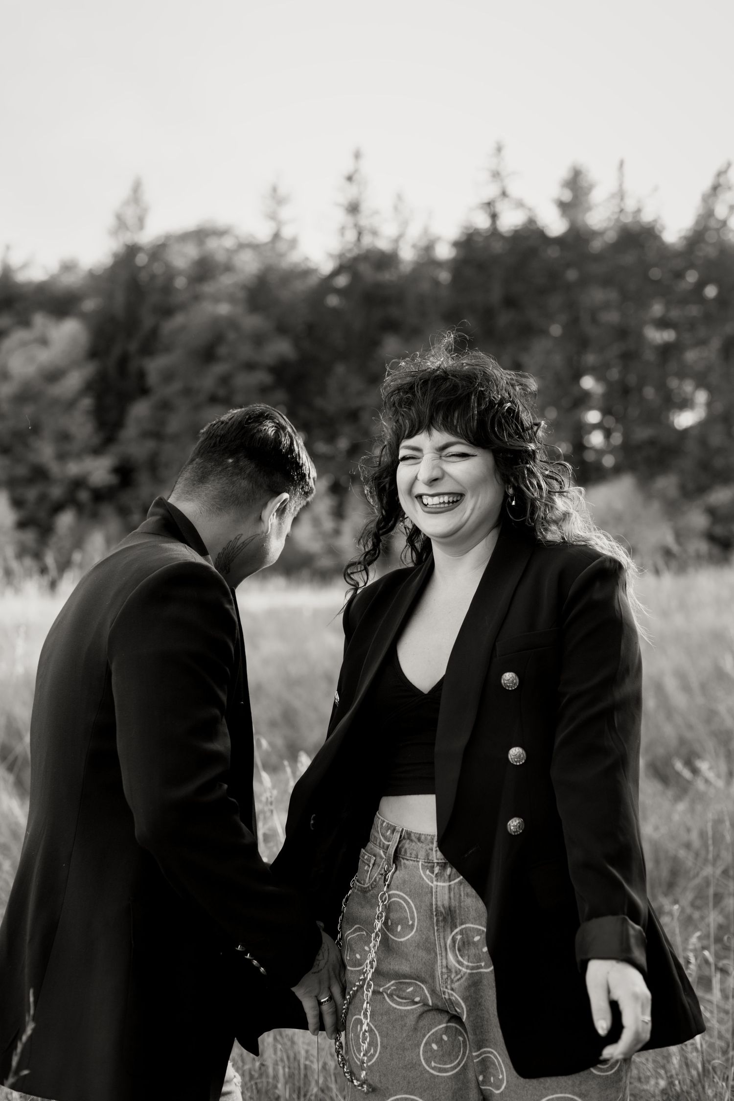 Black and white photo of smiling woman in black blazer laughing with partner in outdoor field setting.