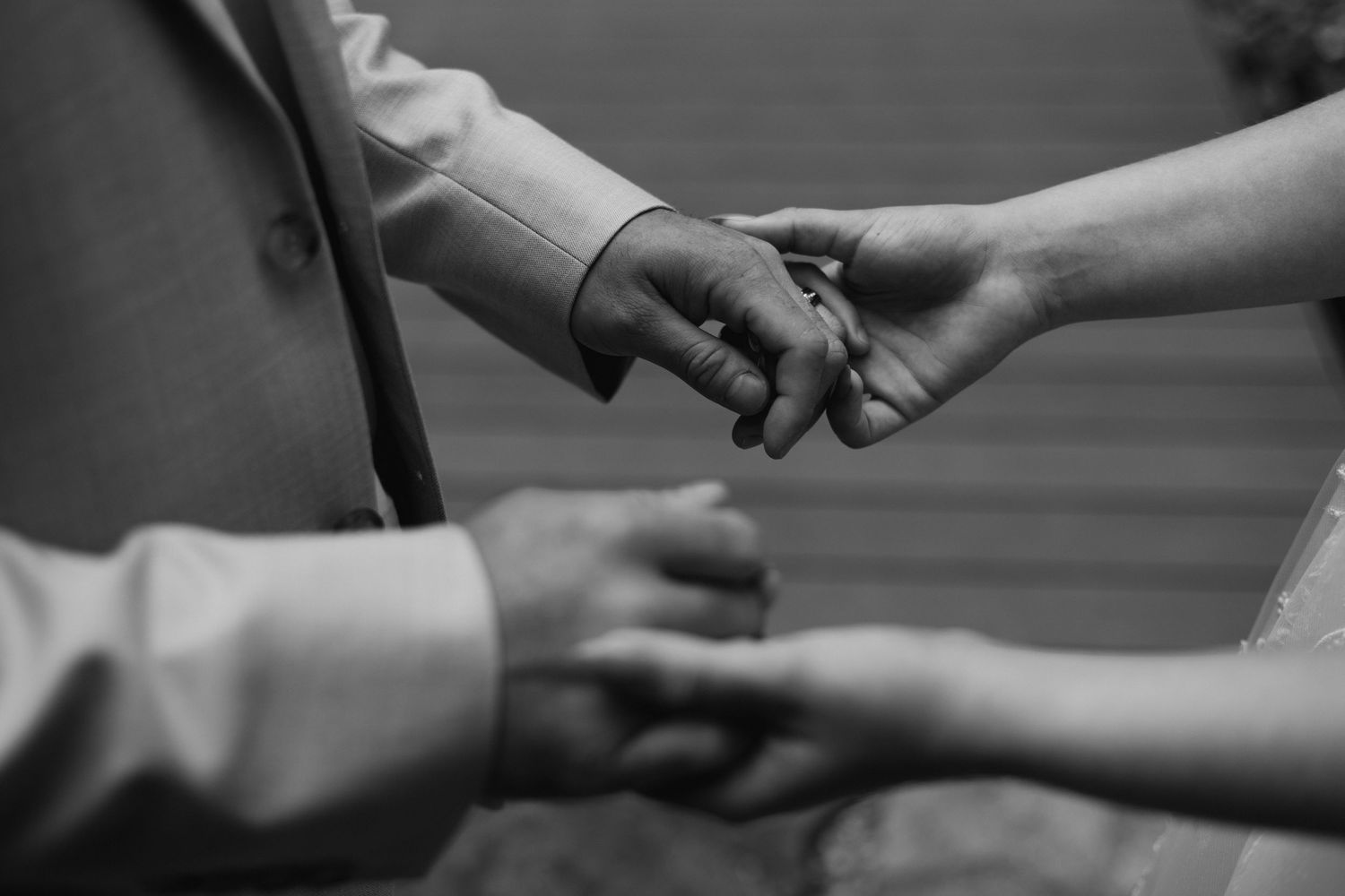 Black and white close-up of bride and groom holding hands during intimate wedding moment.