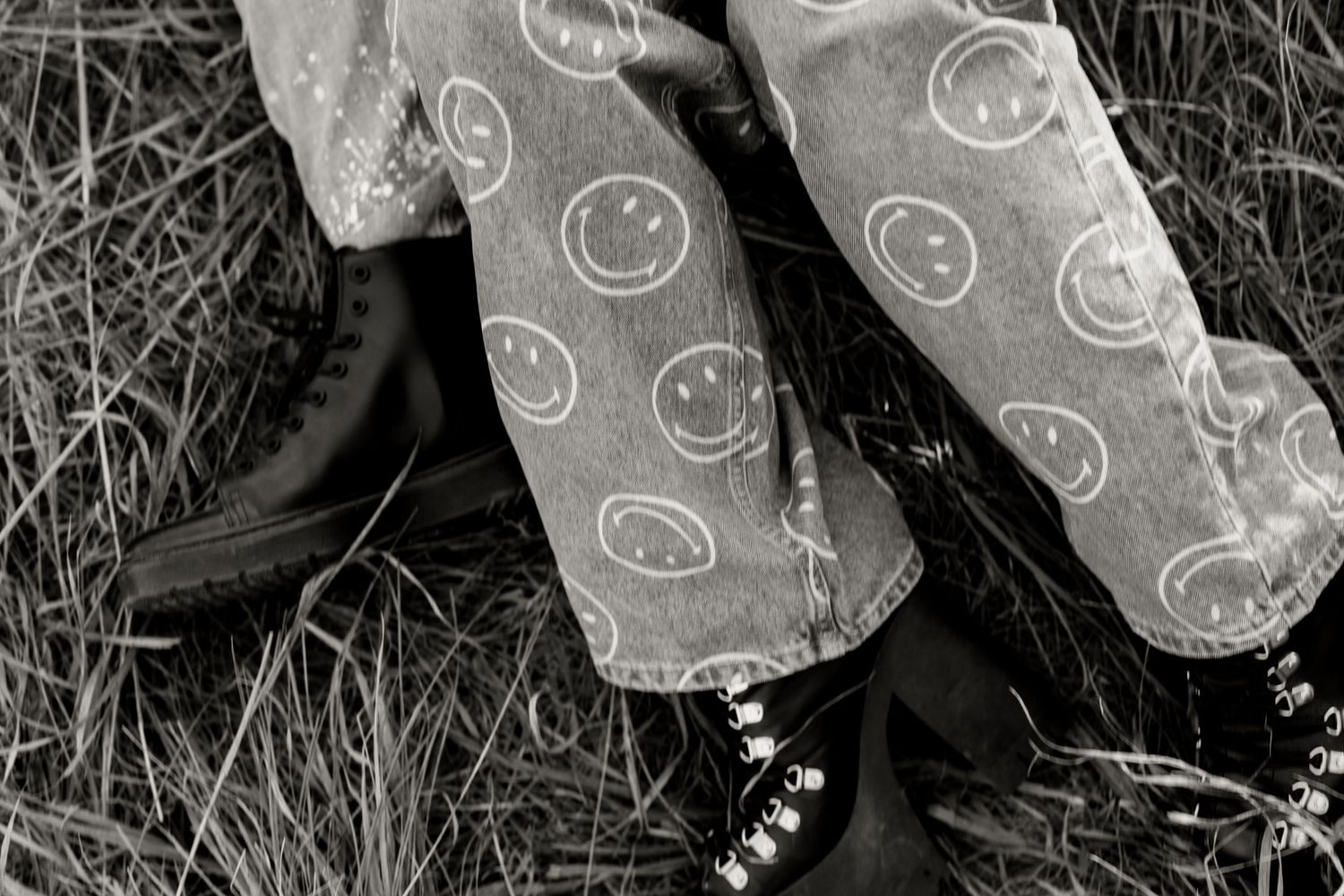 Black and white close-up of smiley face jeans and boots in tall grass.
