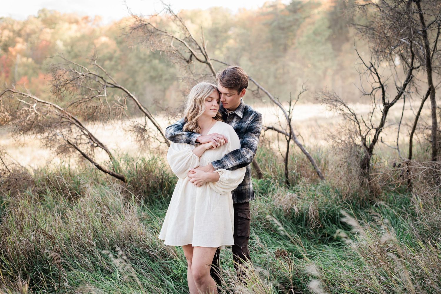 Couple embracing in golden autumn field during outdoor engagement photo session.