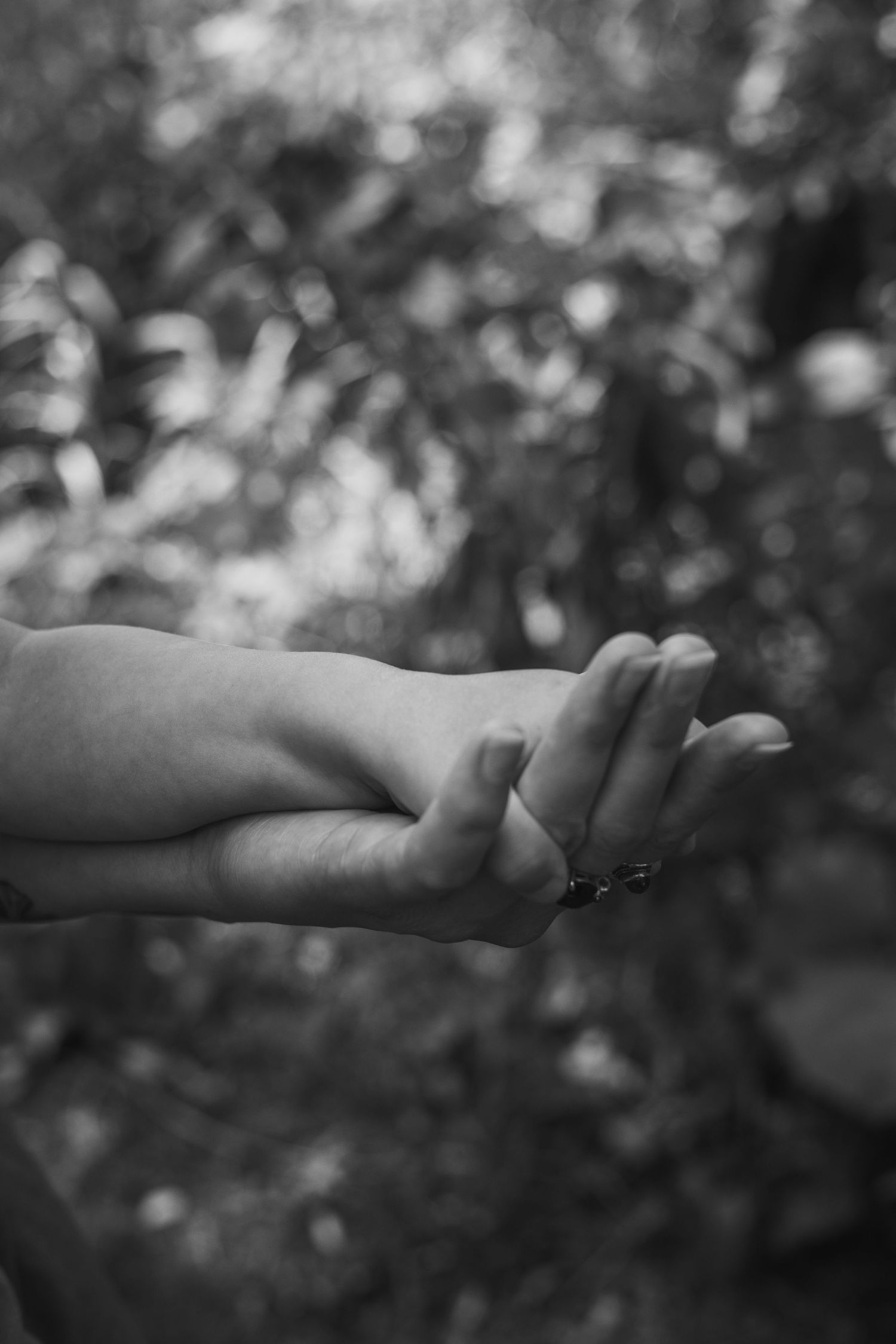 Black and white close-up of a mother and child holding hands together in an outdoor setting.