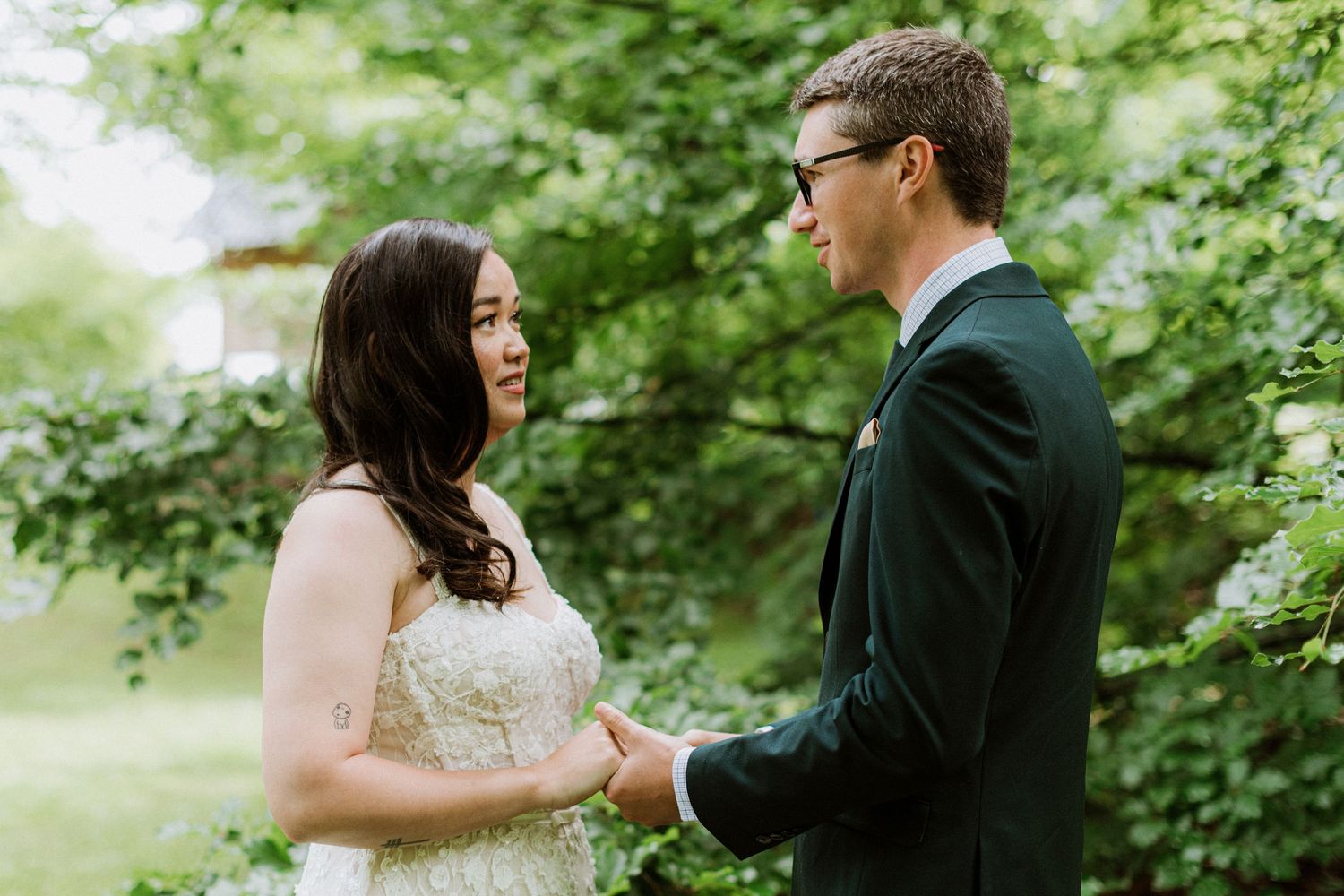 Couple shares an intimate moment holding hands and smiling at each other surrounded by green foliage.