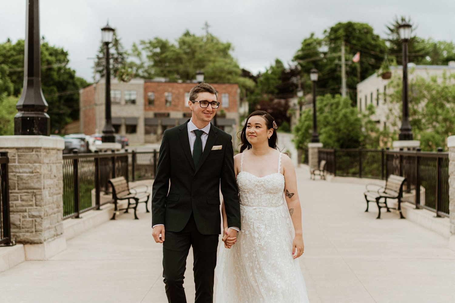 Bride and groom walk hand in hand on a bridge in an outdoor urban setting on their wedding day.